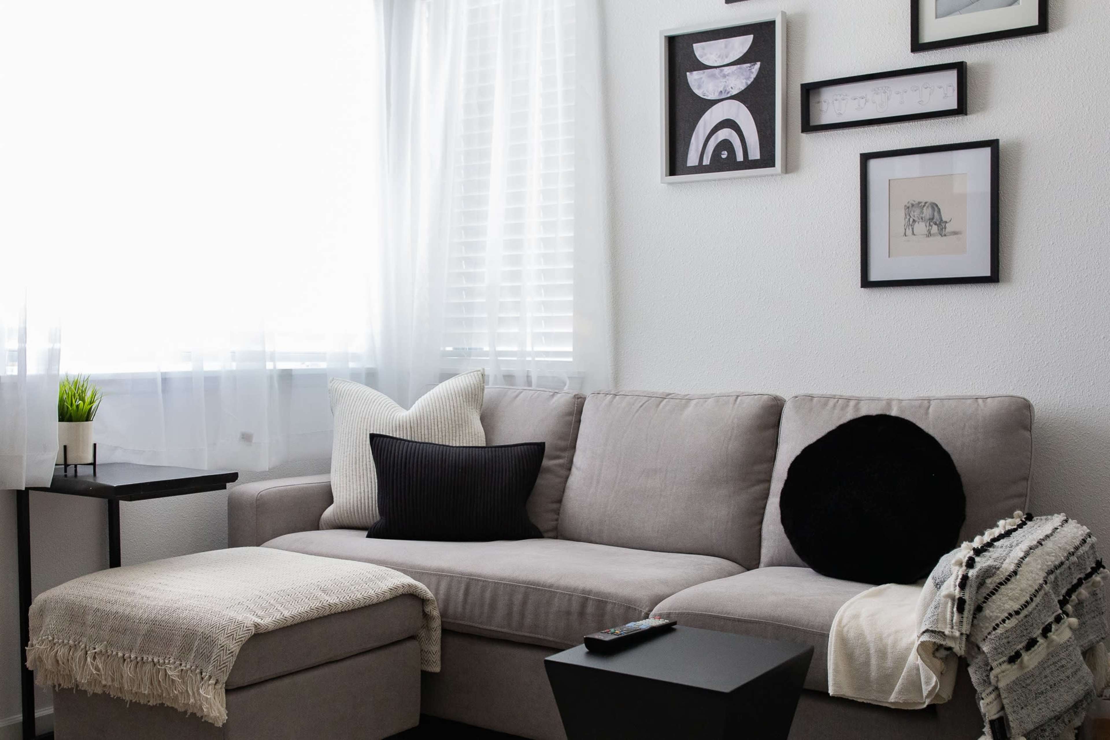 A light-colored living room with a grey couch, decorative pillows, a small side table, and wall art.