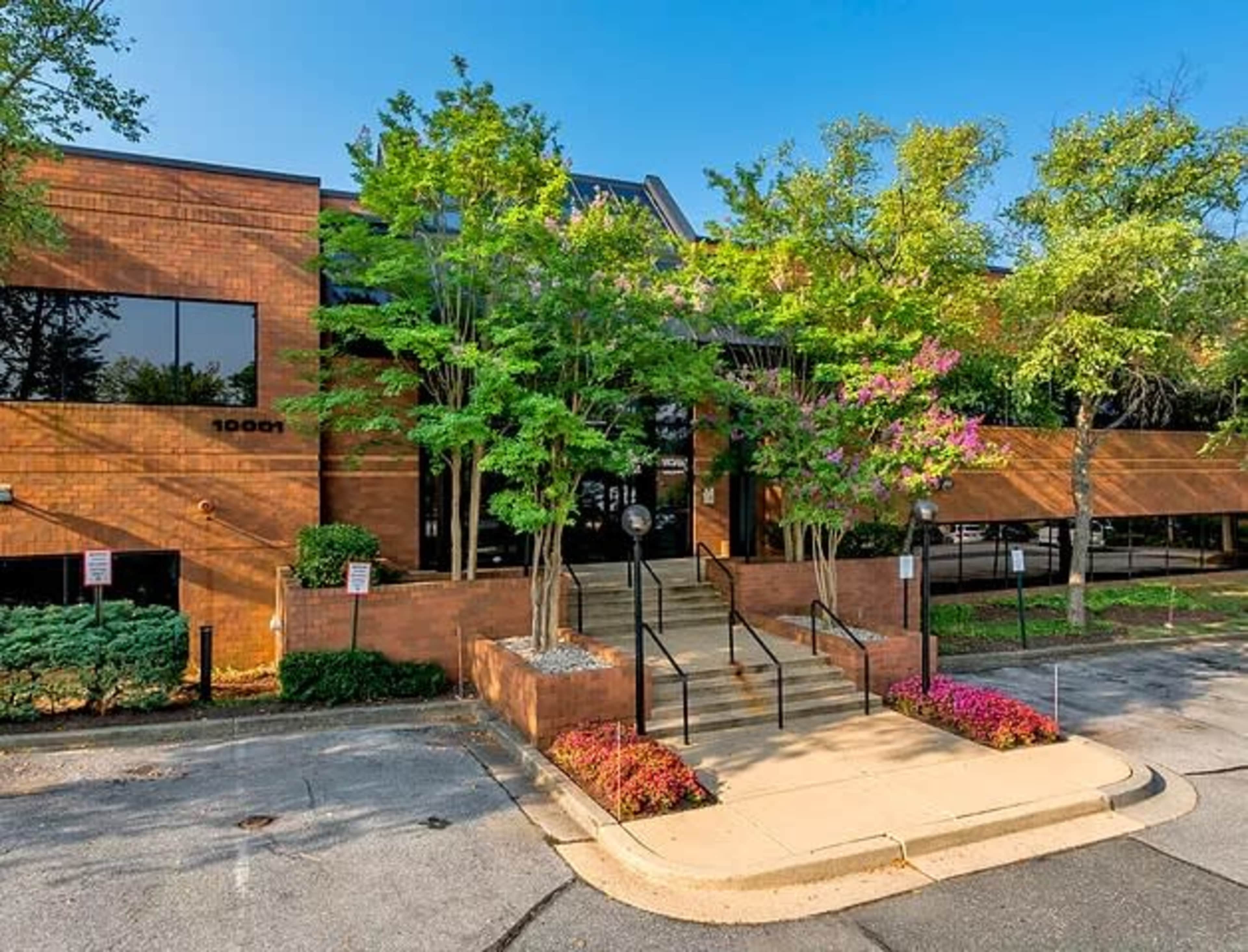 A modern brick office building with a landscaped entrance featuring steps and flowering plants.