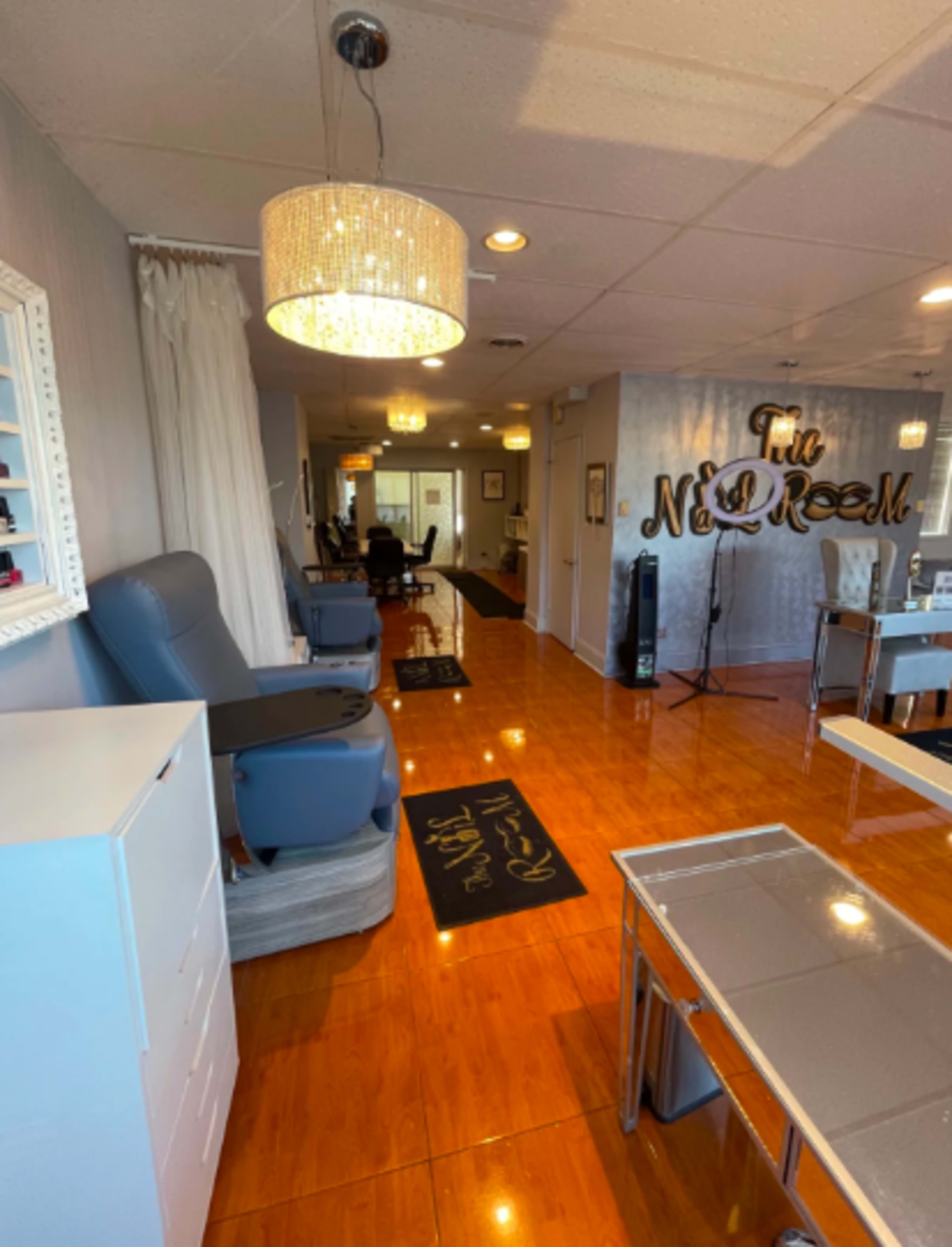 The image shows a brightly lit nail salon with modern furnishings, including pedicure chairs and a reception area featuring the salon's name on the wall.