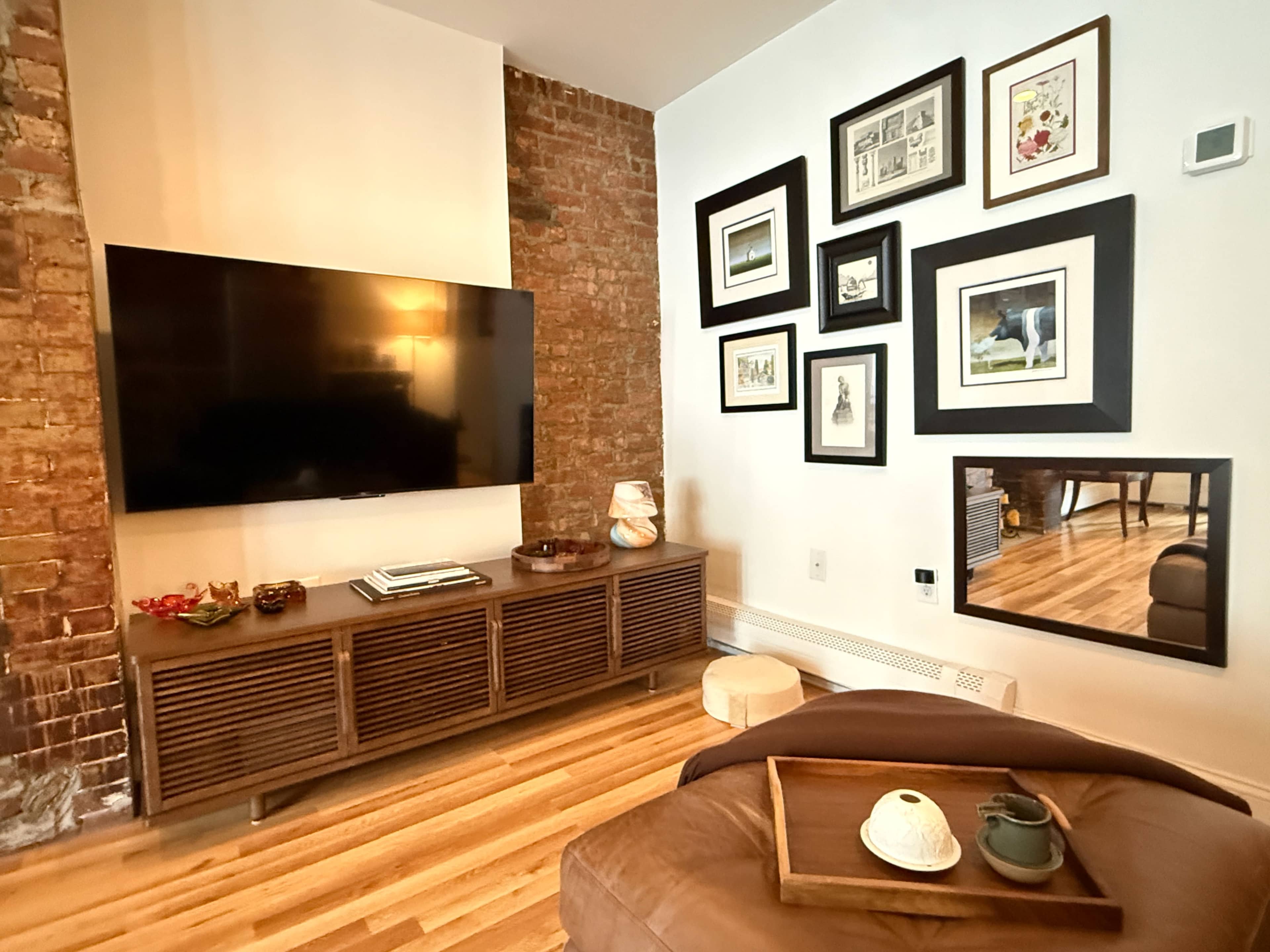 A living room features a large wall-mounted television above a wooden media console, with a gallery of framed artworks displayed on the adjacent wall.