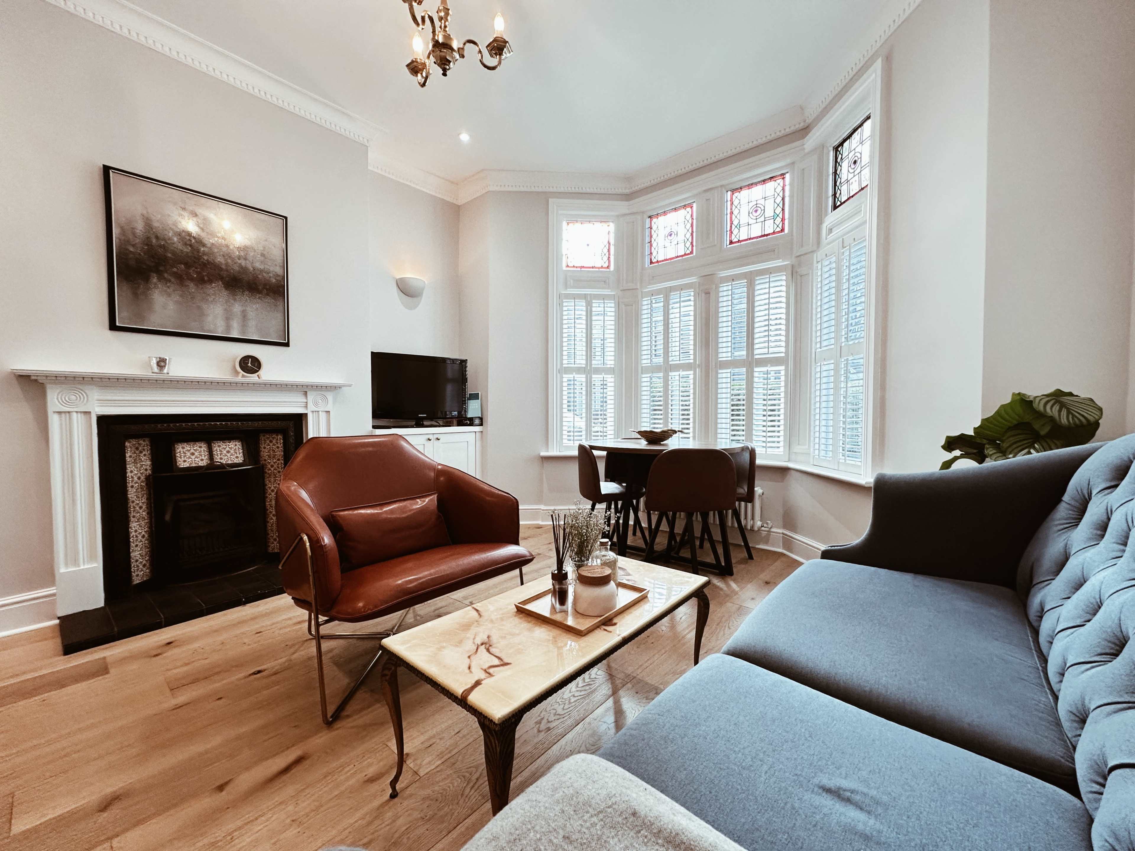 A bright living room featuring a blue sofa, a brown armchair, a wooden coffee table, and a bay window with stained glass.
