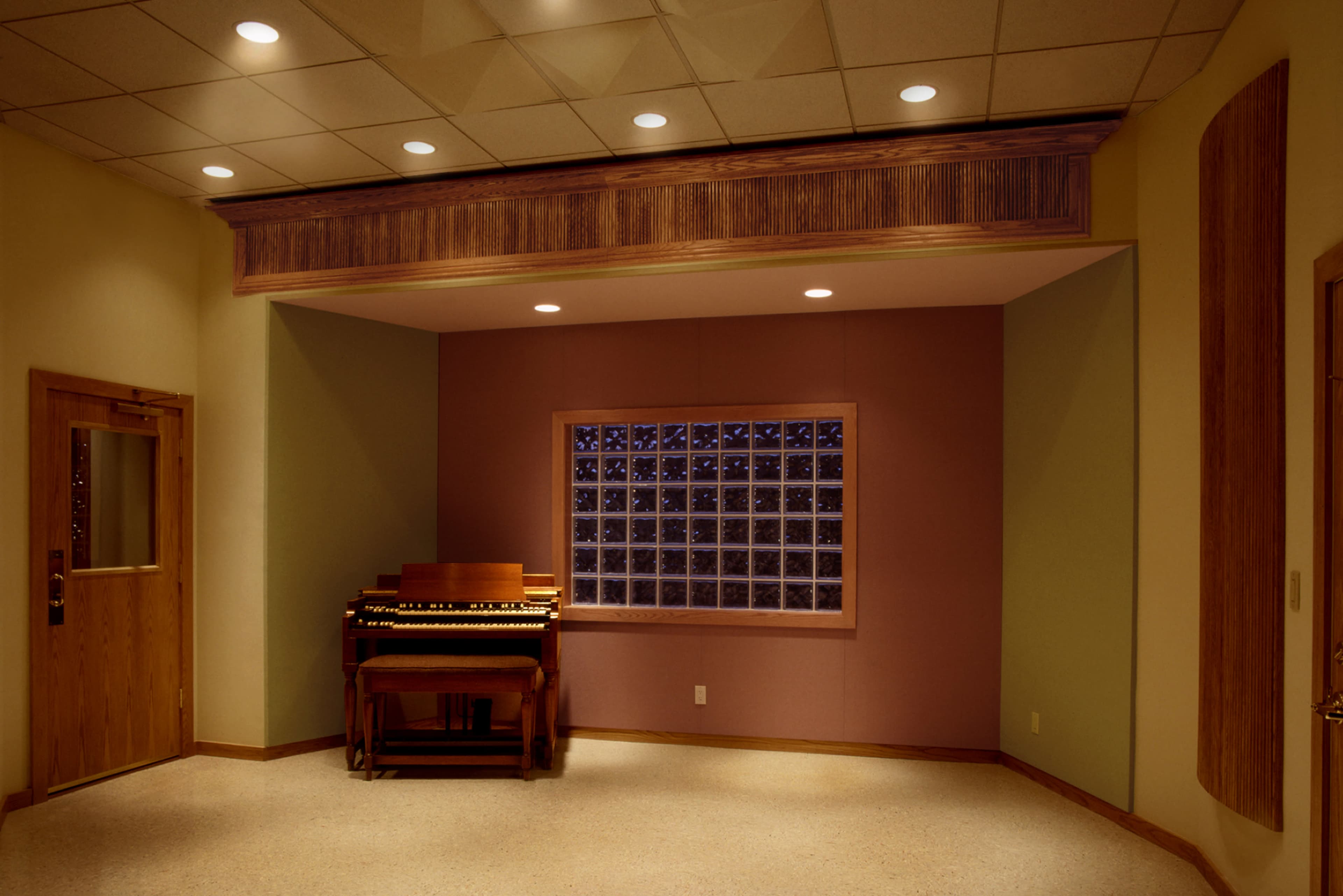A small studio room featuring a wooden organ beside a large window with a grid of small glass panes.