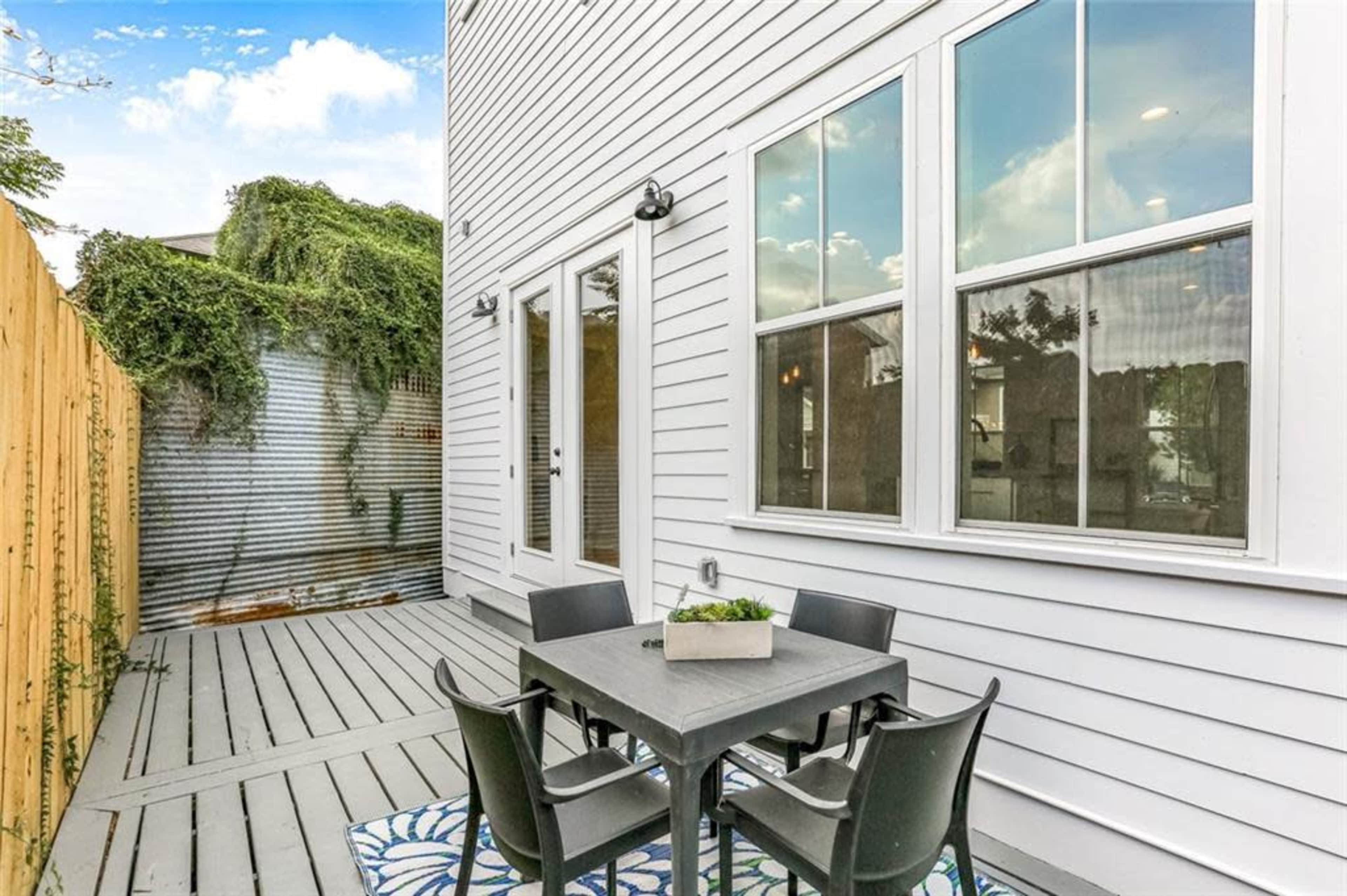 A patio area with a table and four chairs adjacent to a wall with greenery and a corrugated metal surface.