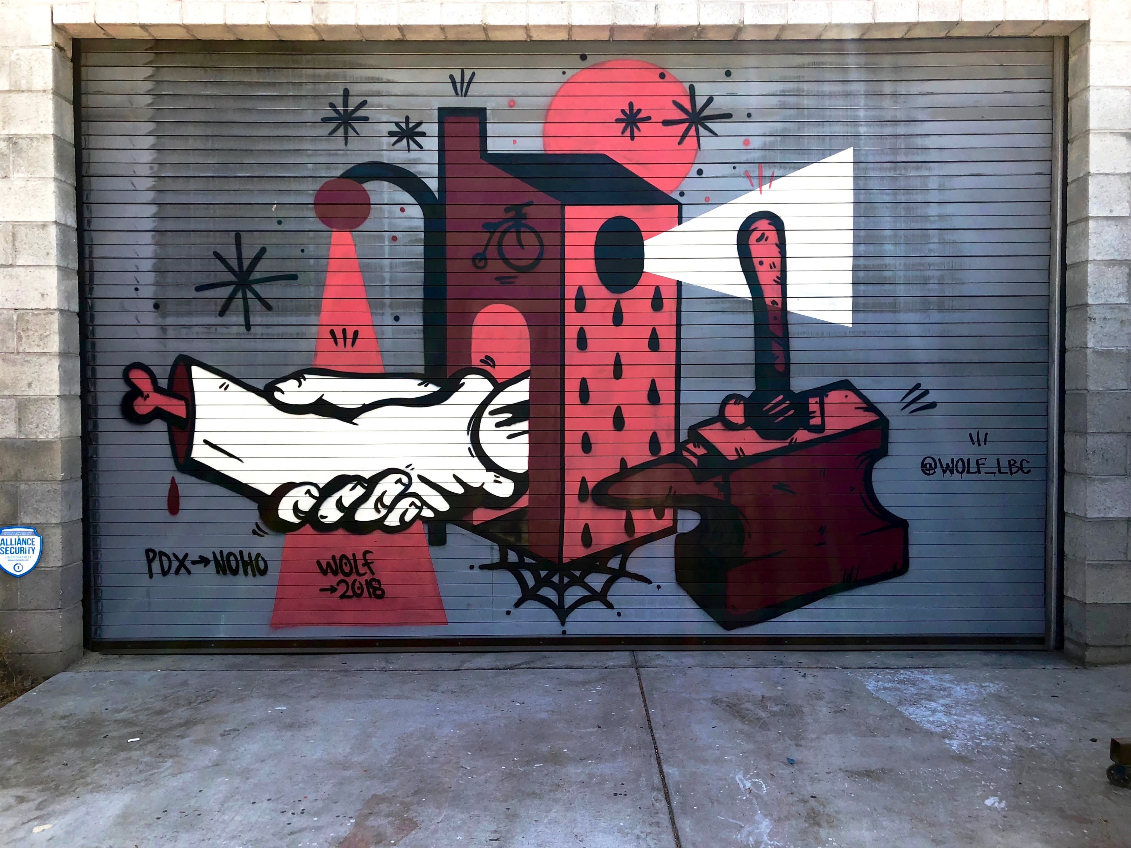 A vibrant mural on a garage door, depicting a hand passing a stylized object with geometric shapes and bold colors.