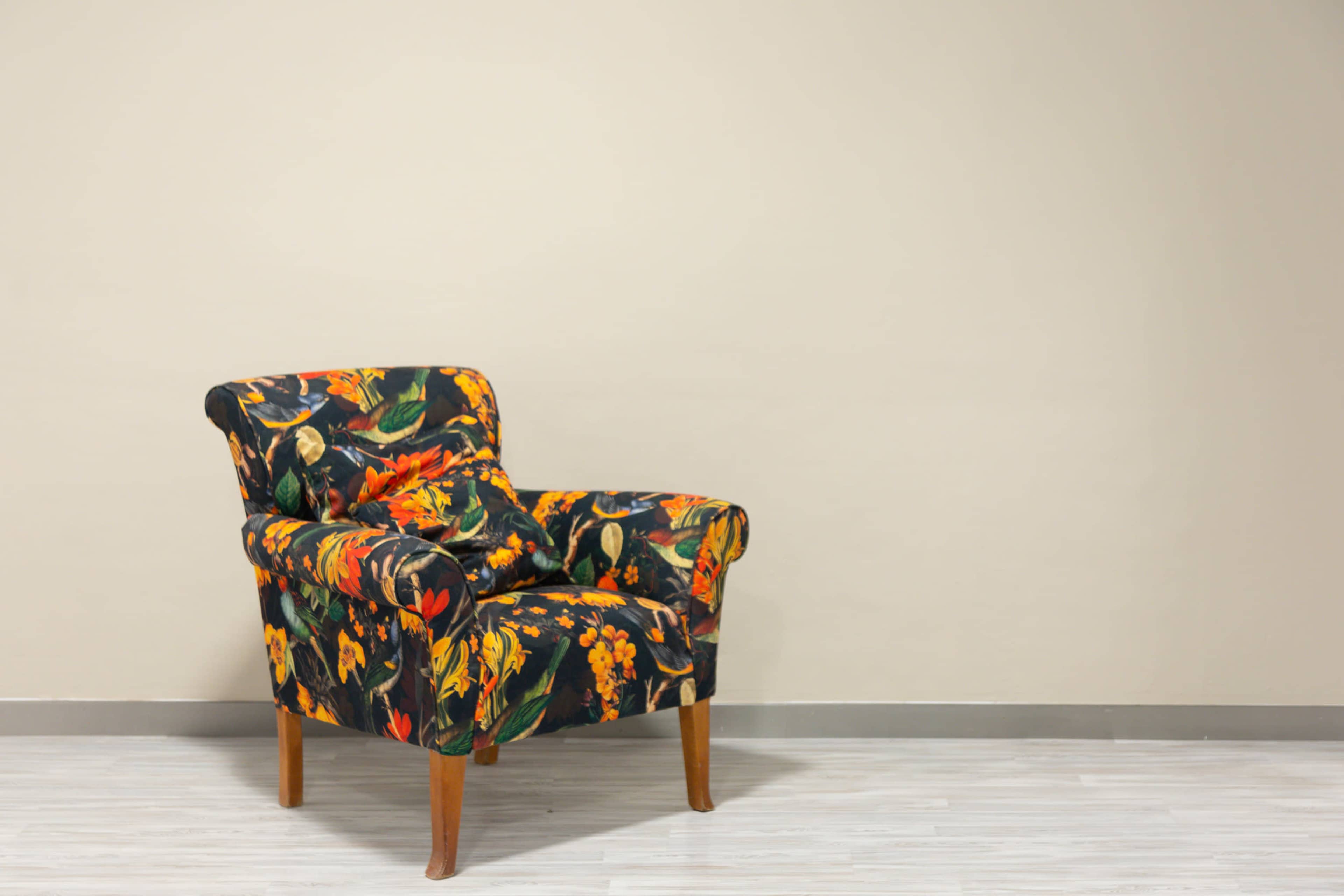 A floral-patterned armchair with wooden legs is positioned against a light-colored wall.