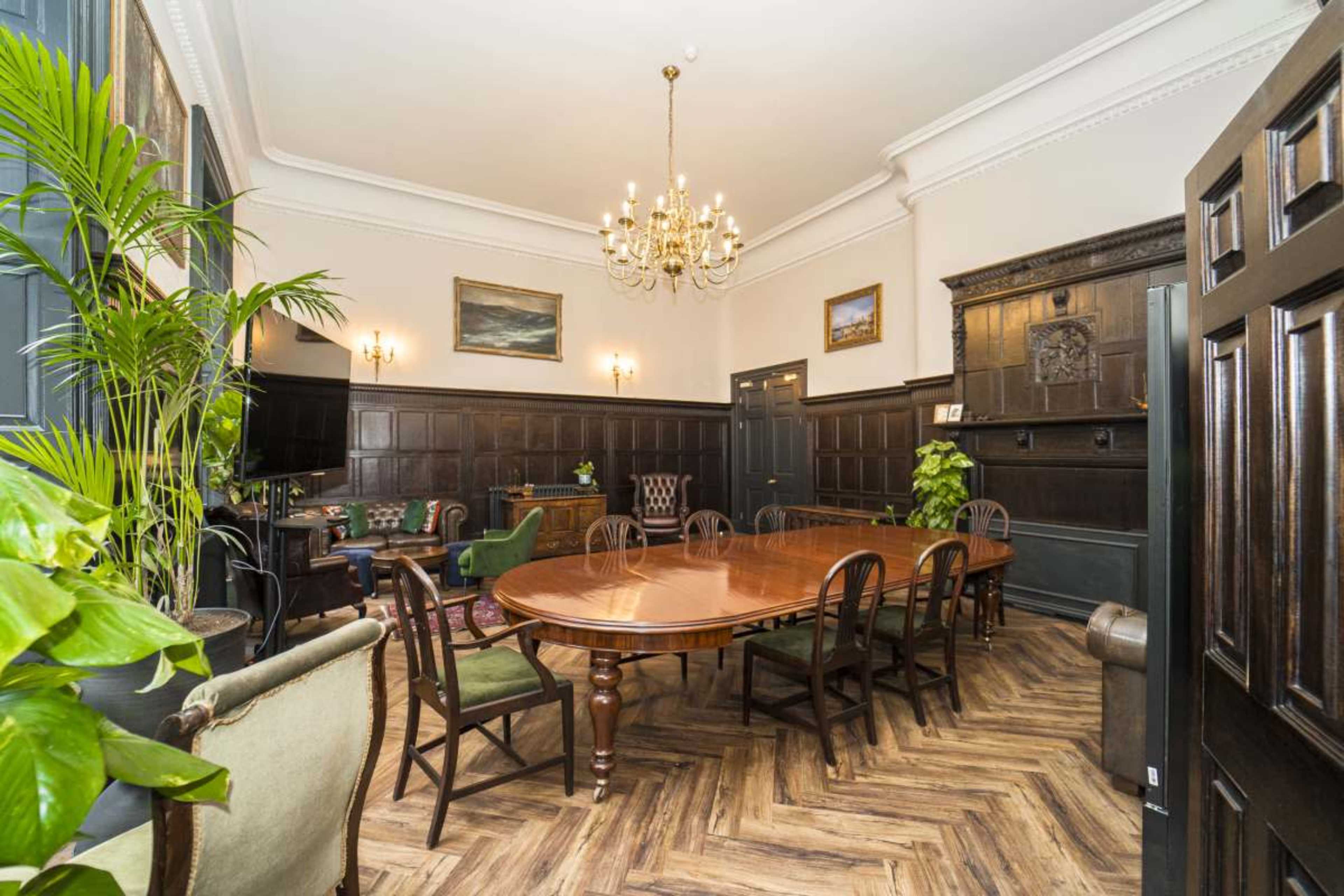 The image shows a richly appointed conference room with a large wooden table surrounded by chairs, adorned with decorative plants and framed artwork on the walls.