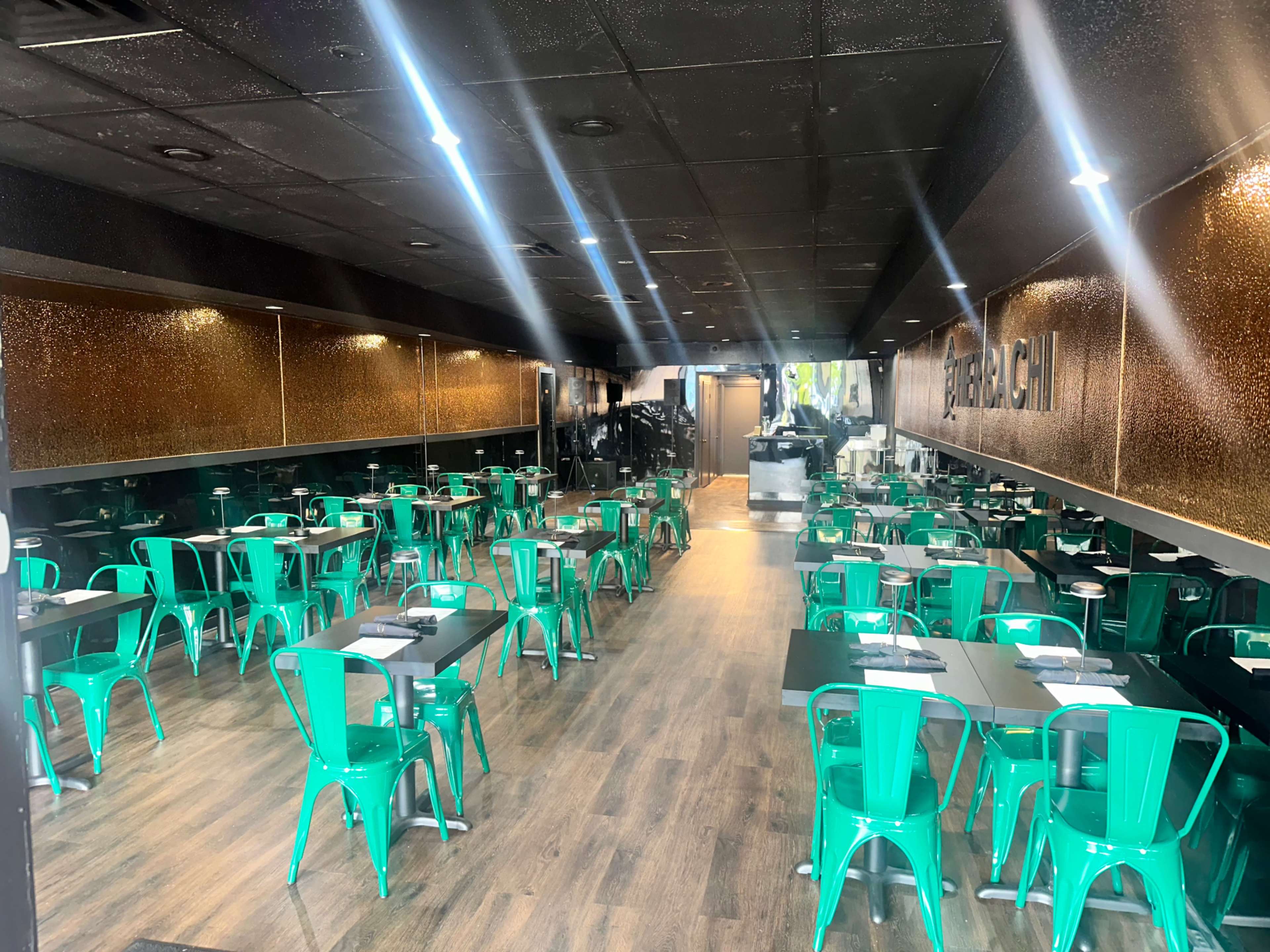 The image shows a modern restaurant interior with green metal chairs and black tables arranged in a spacious layout.