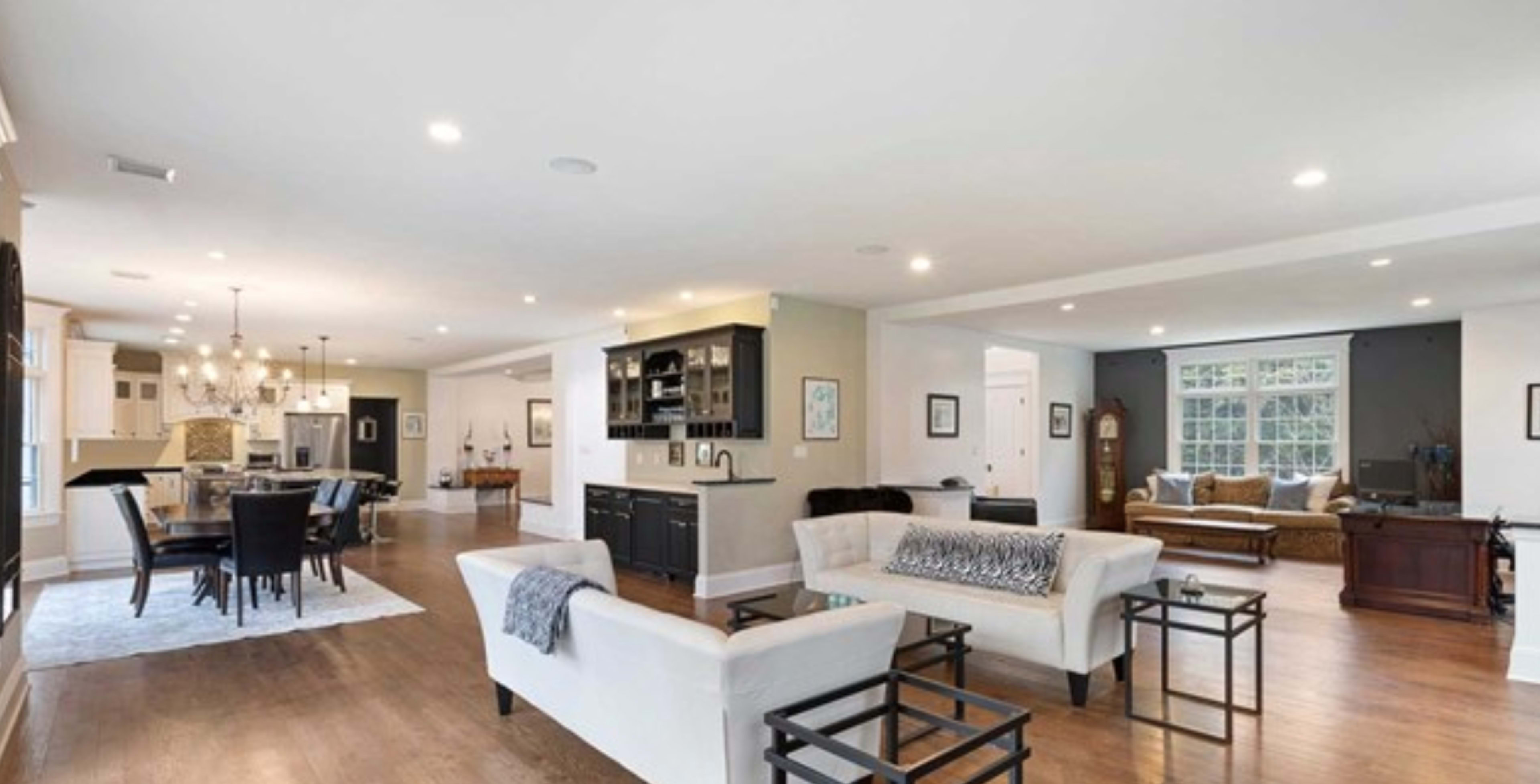 A spacious, modern open-concept living area with a living room, dining area, and kitchen, featuring light-colored furniture and hardwood floors.