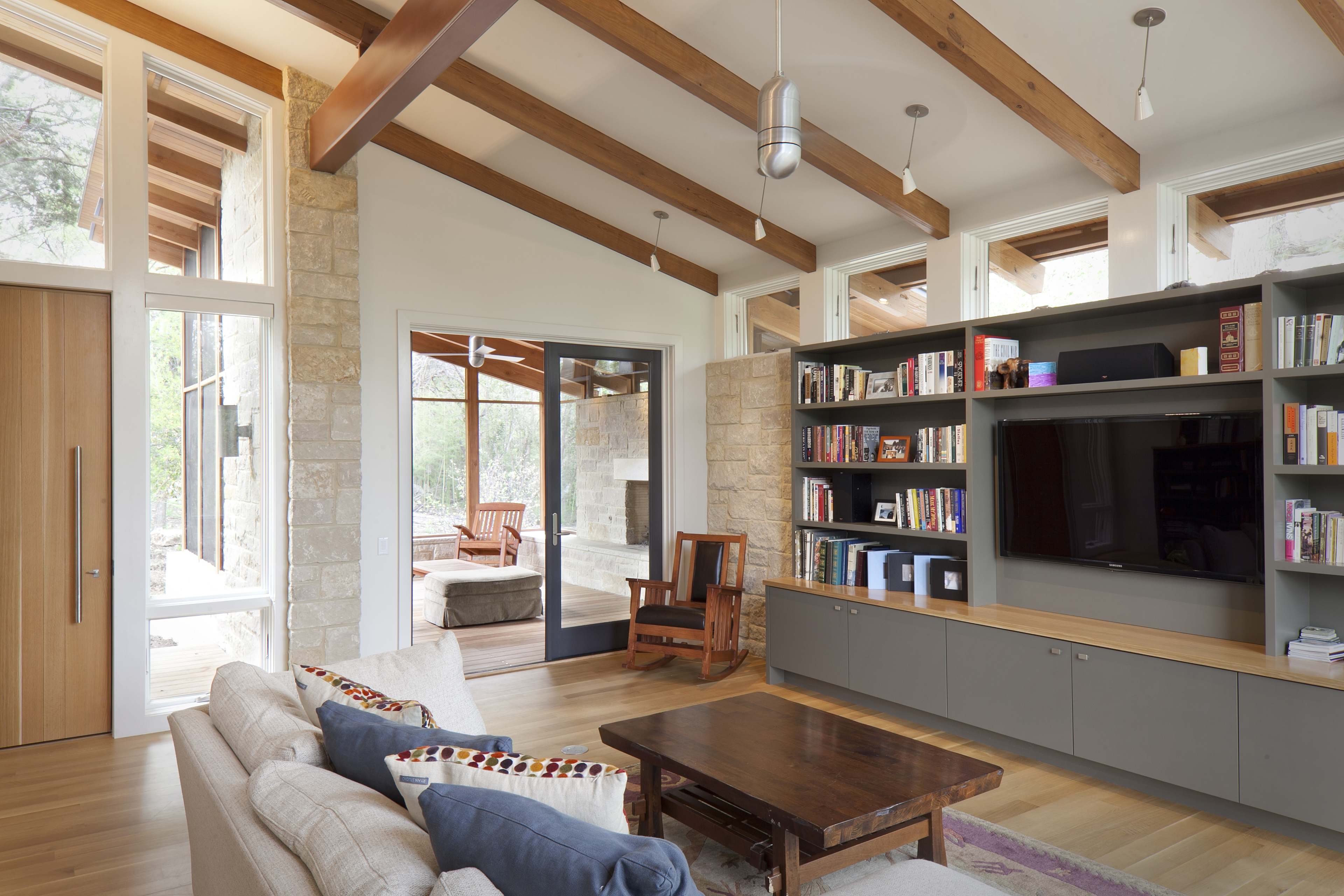 A modern living room with large windows, wooden beams, a built-in bookshelf, and a comfortable seating arrangement.