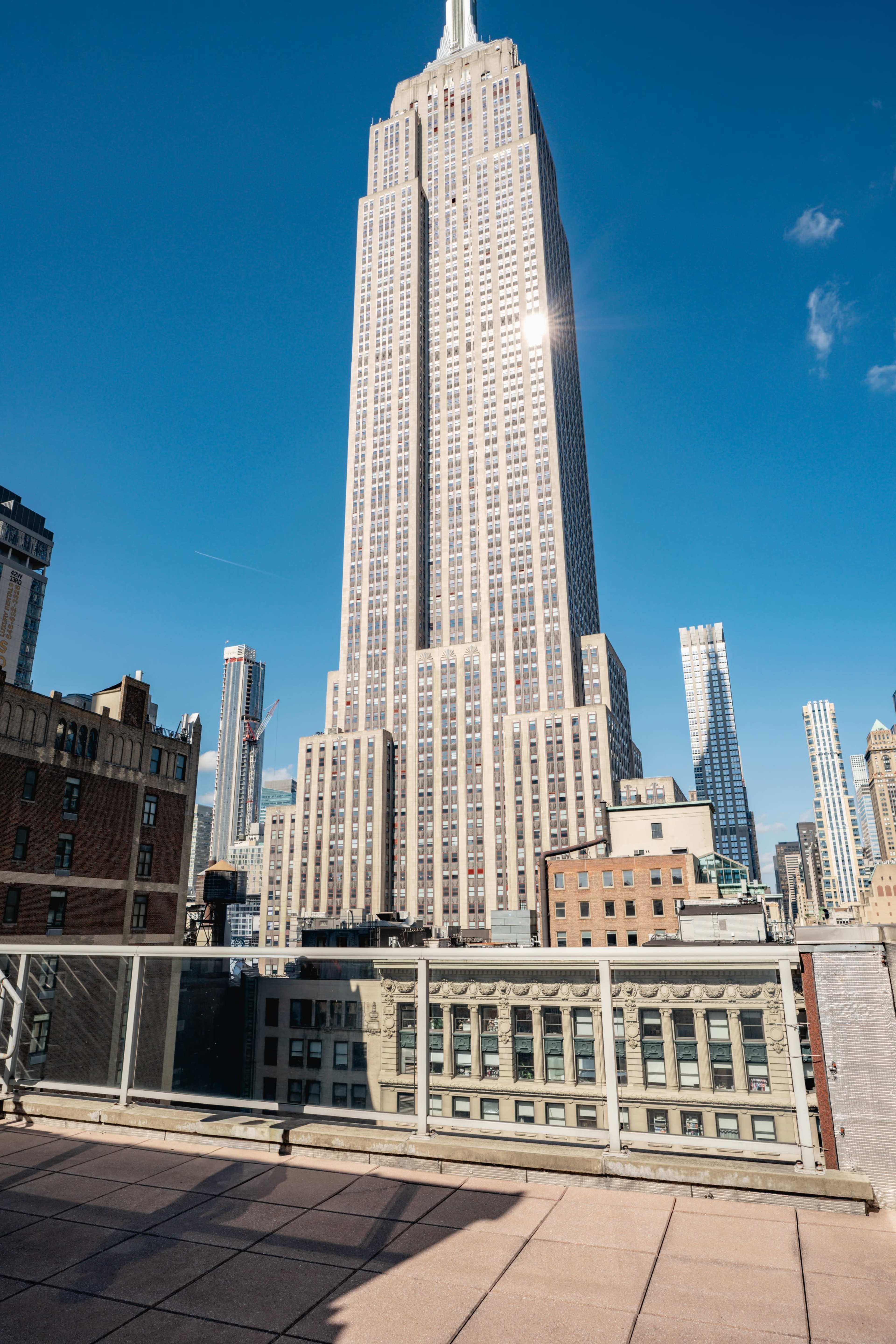 The image shows the Empire State Building towering above the surrounding buildings against a clear blue sky.