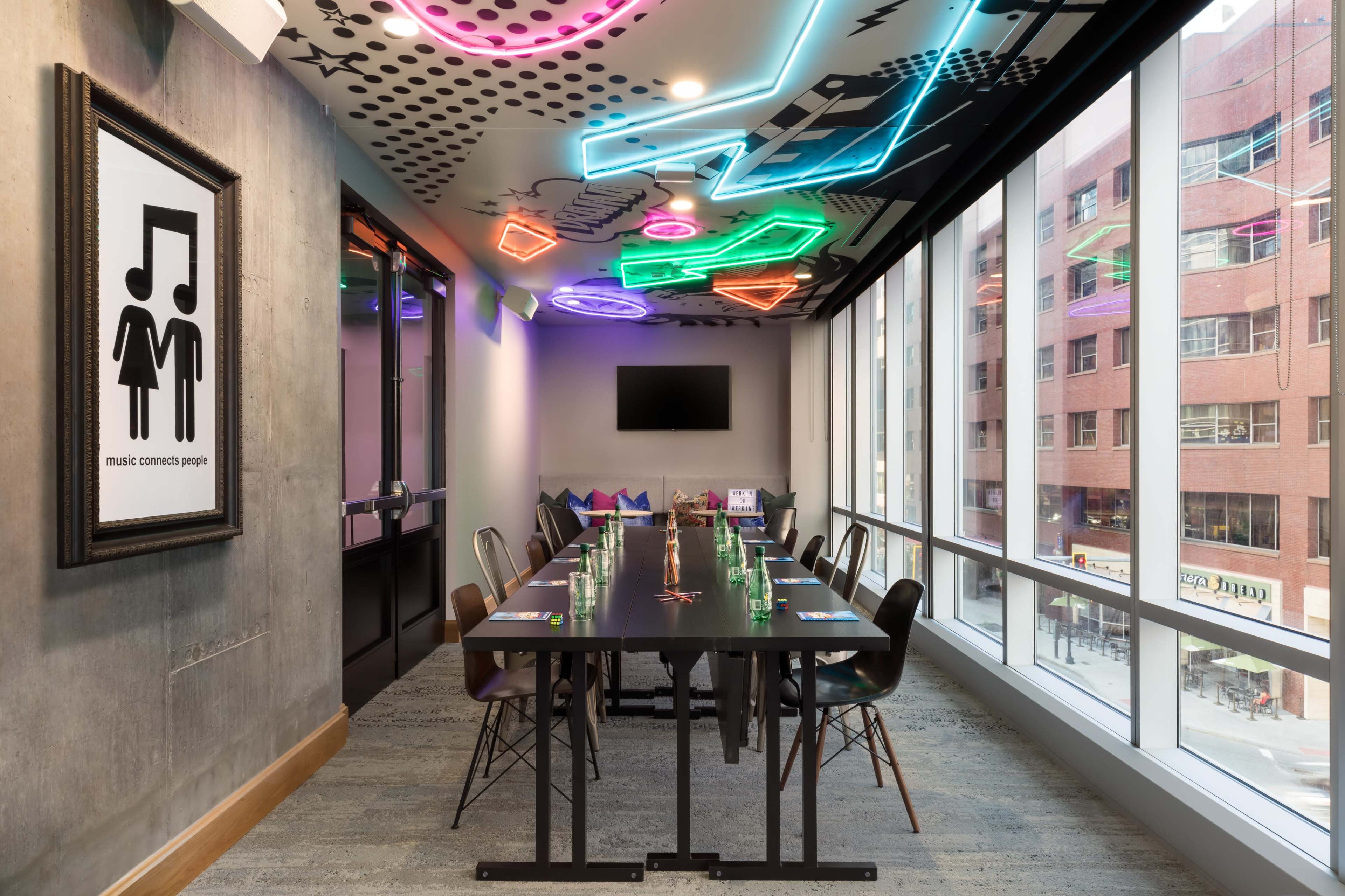 A meeting room features a long black table surrounded by chairs, with colorful neon lights and a wall art piece emphasizing the theme of music.
