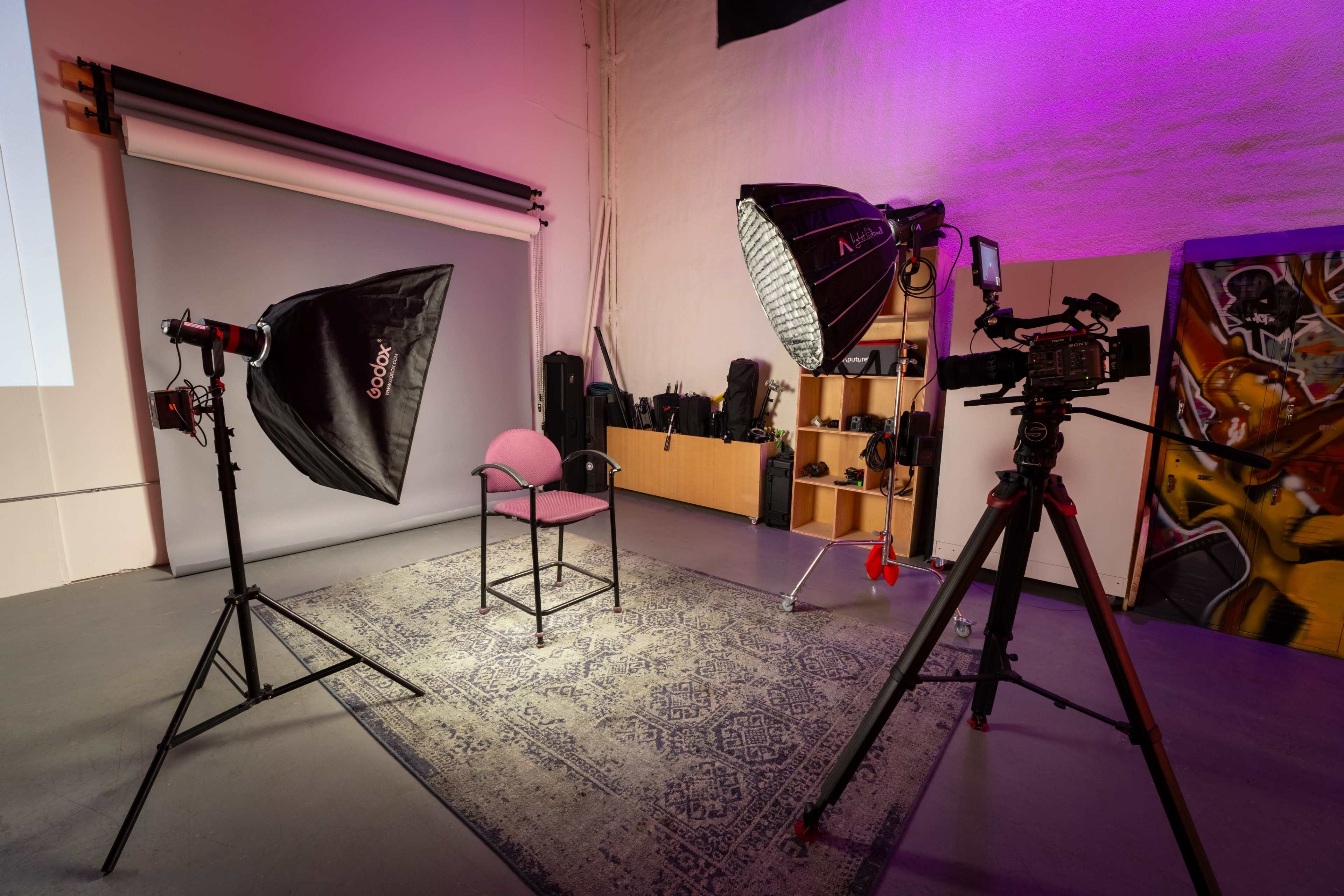 A photography studio setup with a central chair, softbox lights, a camera on a tripod, and equipment displayed in the background.