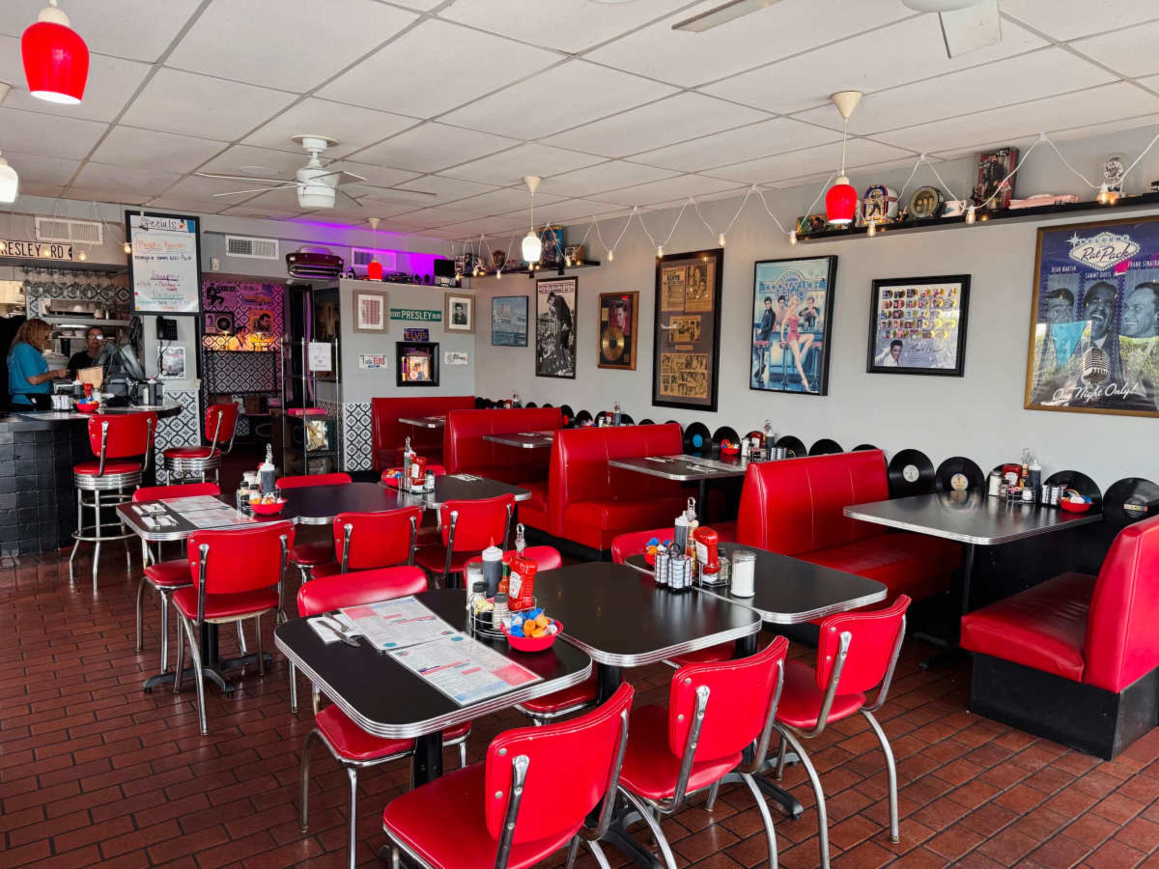 The image shows a vintage-style diner interior with red booths, black tables, and framed artwork on the walls.