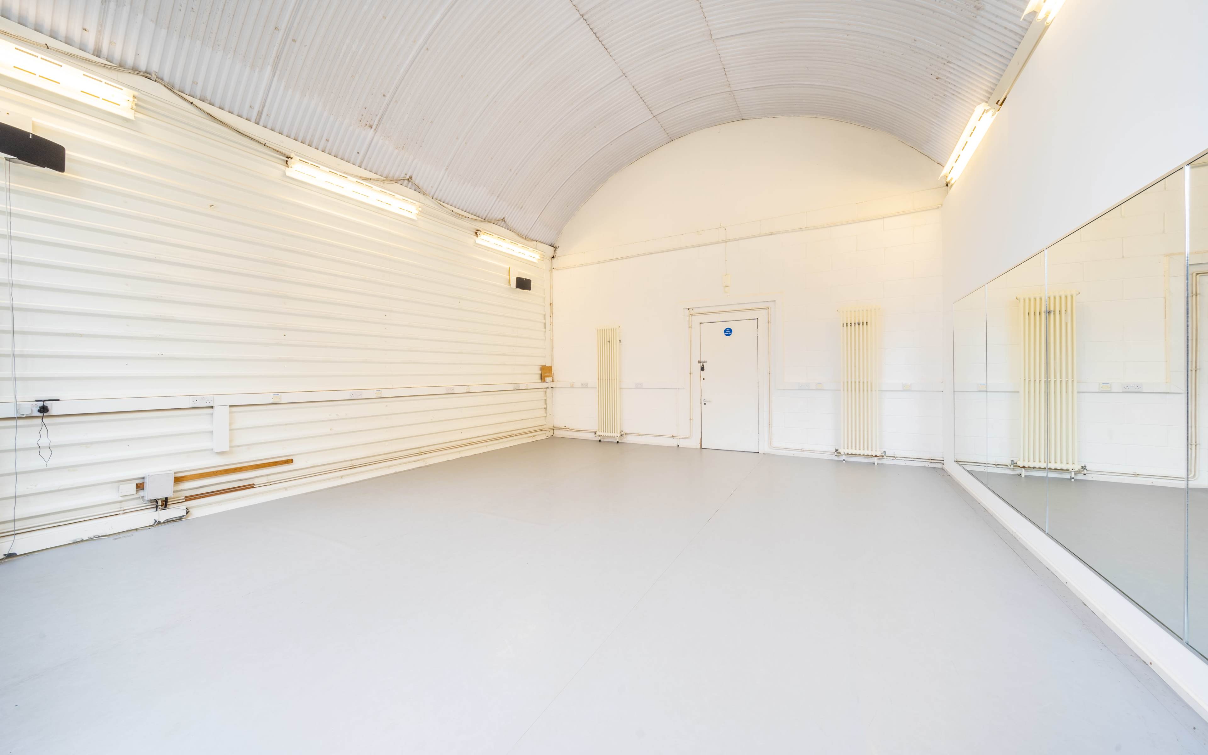A spacious dance studio with a mirrored wall and a simple white interior.