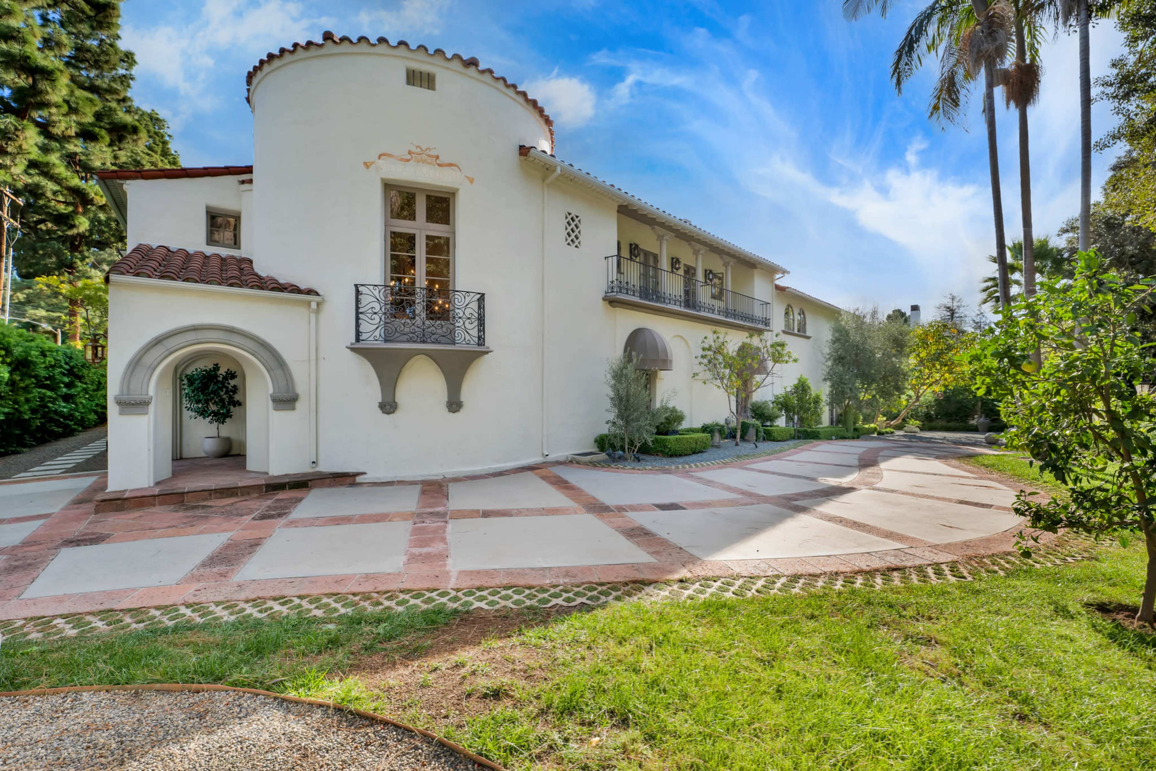 A large, white stucco house with a curved balcony and palm trees in the surrounding garden.