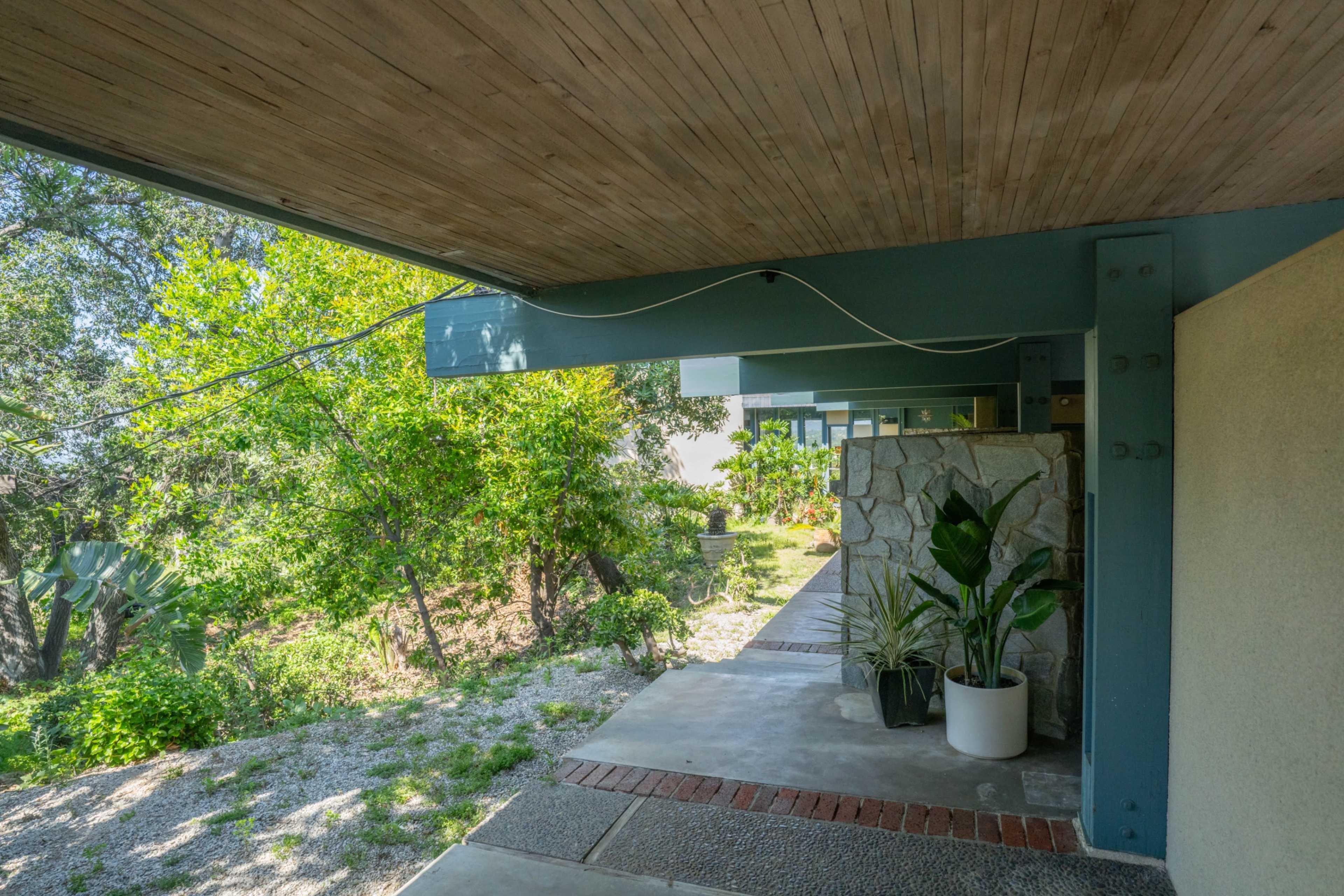 A covered walkway leads to a modern building, surrounded by greenery and landscaped rocks.
