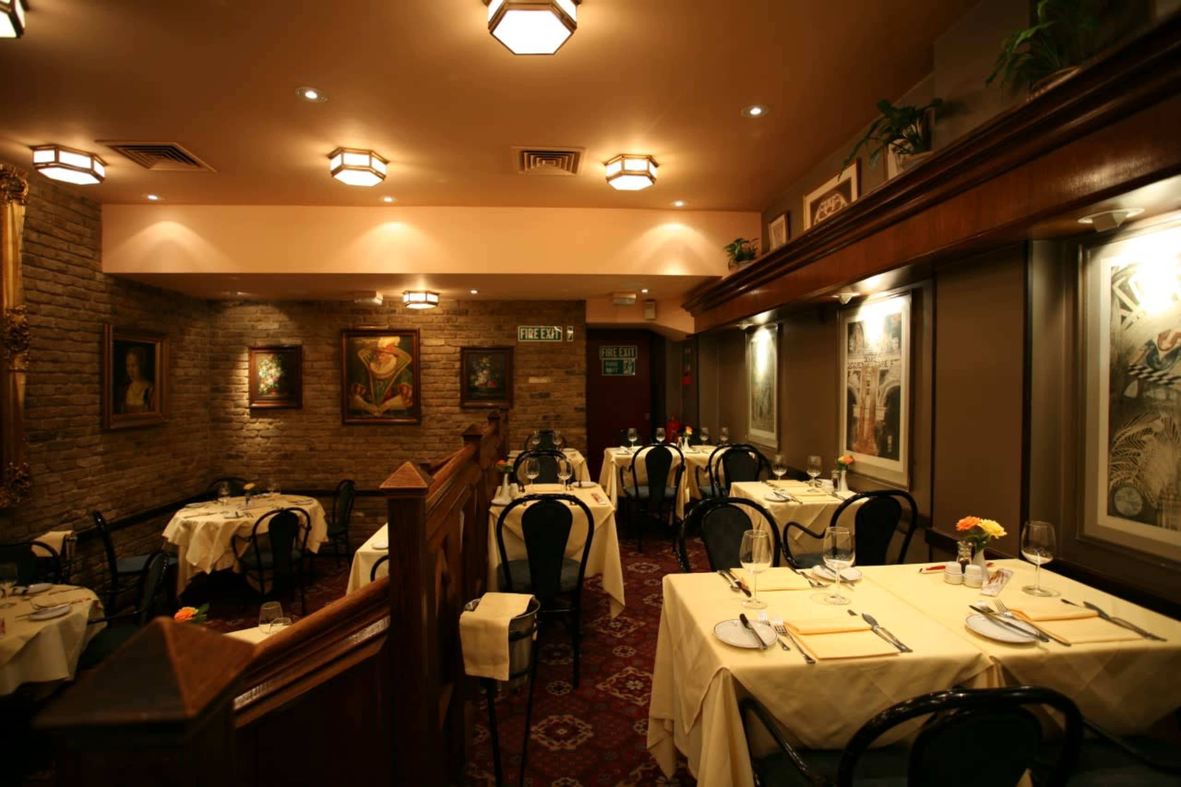 A cozy restaurant interior with tables set for dining, featuring brick walls and decorative art pieces.