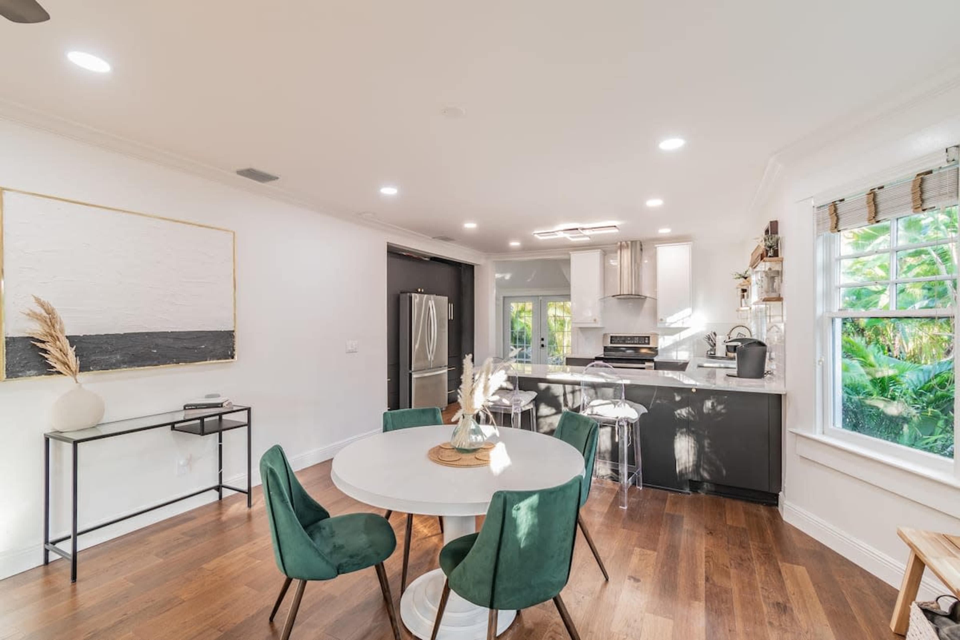 A modern kitchen features a round dining table surrounded by green chairs, with sleek cabinetry and appliances visible in the background.