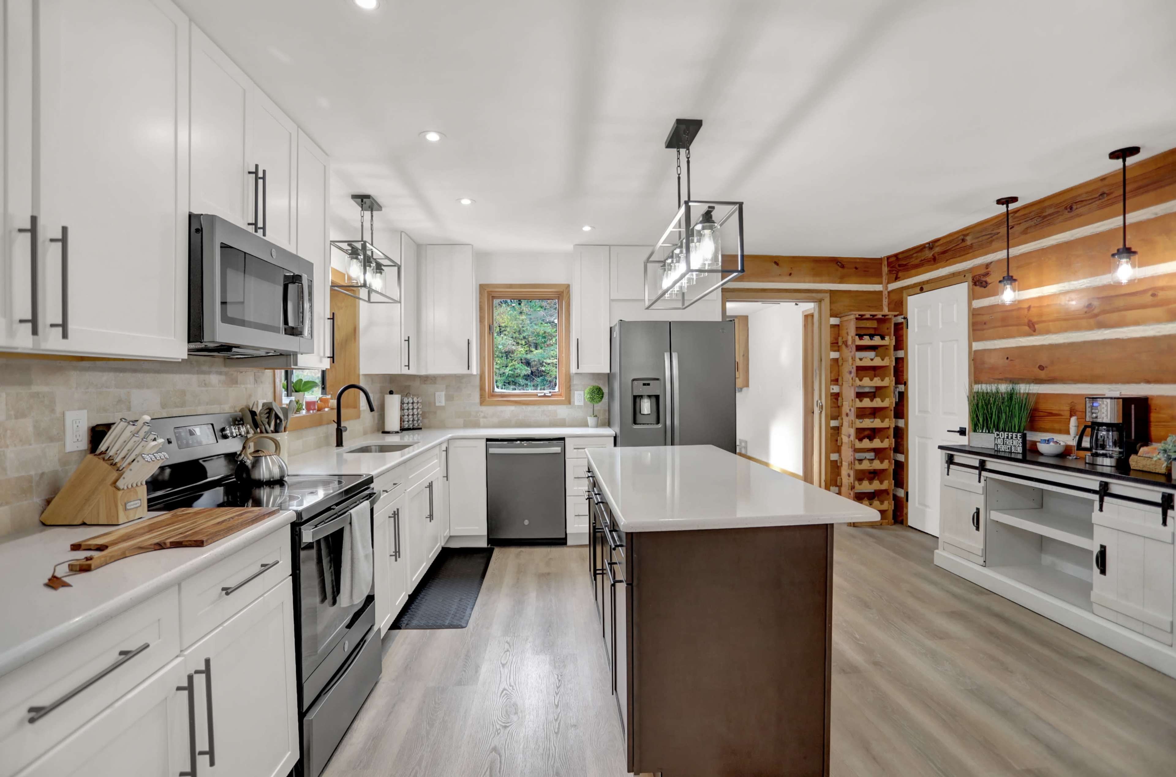 A modern kitchen featuring white cabinetry, stainless steel appliances, a large island with a dark countertop, and wooden accents on the walls.