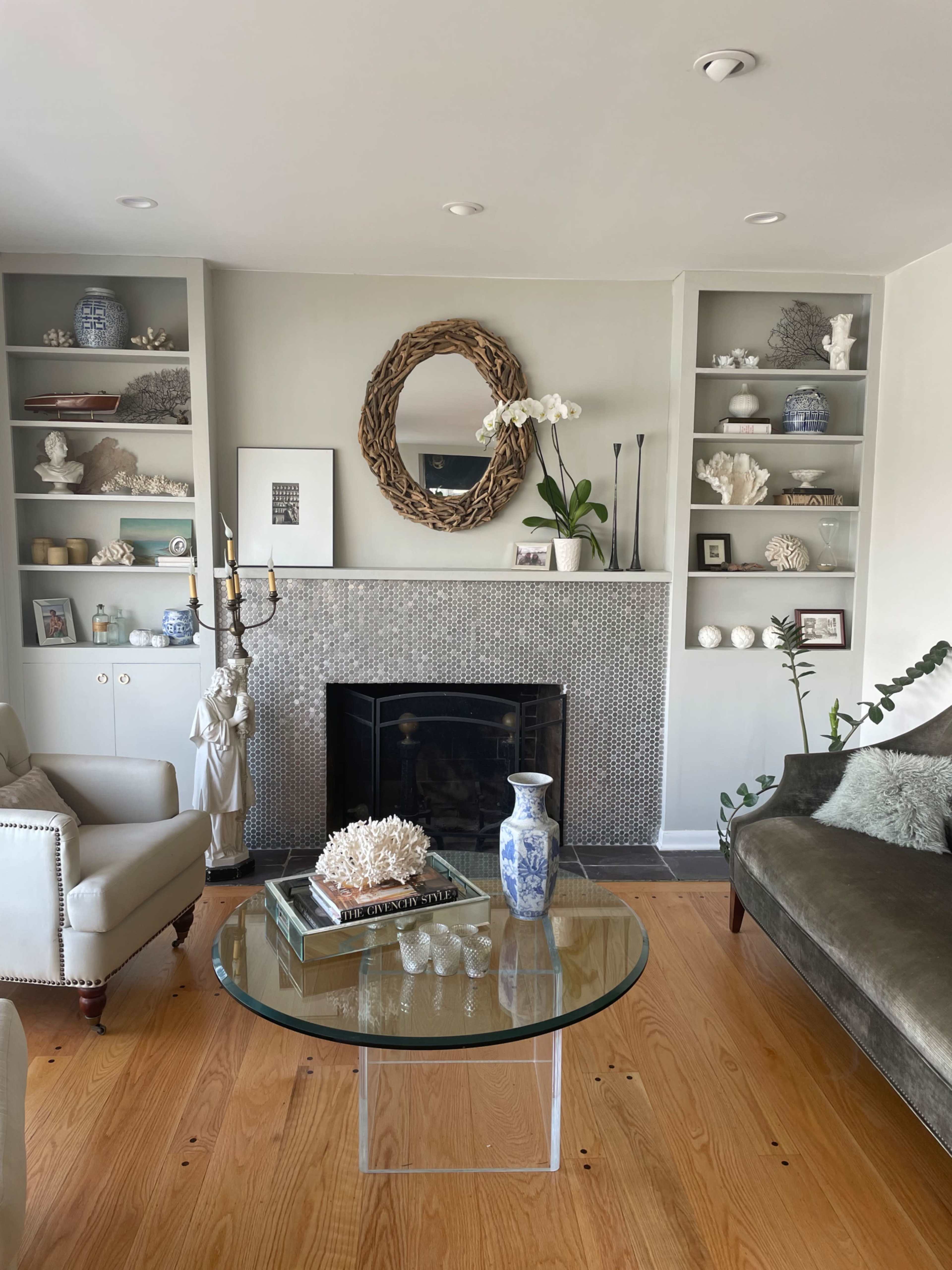 The living room features a fireplace surrounded by shelves displaying various decorative items, with a glass coffee table in the center.