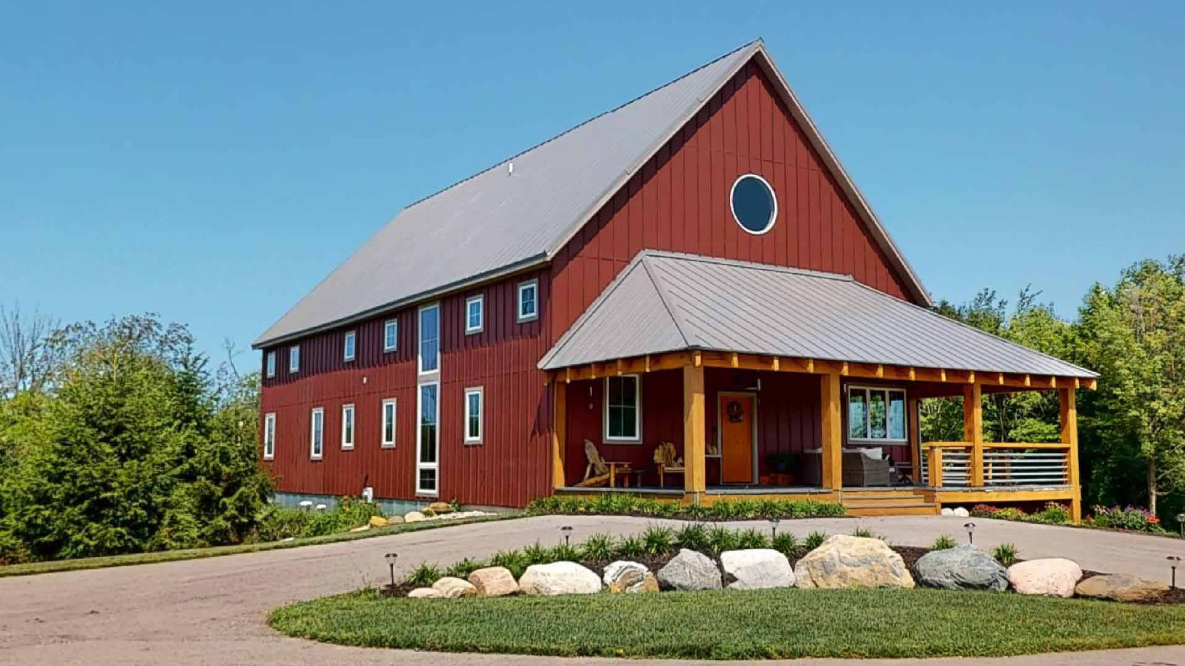 A red barn-style house with a metal roof is set on a landscaped property featuring a circular driveway and a covered porch.