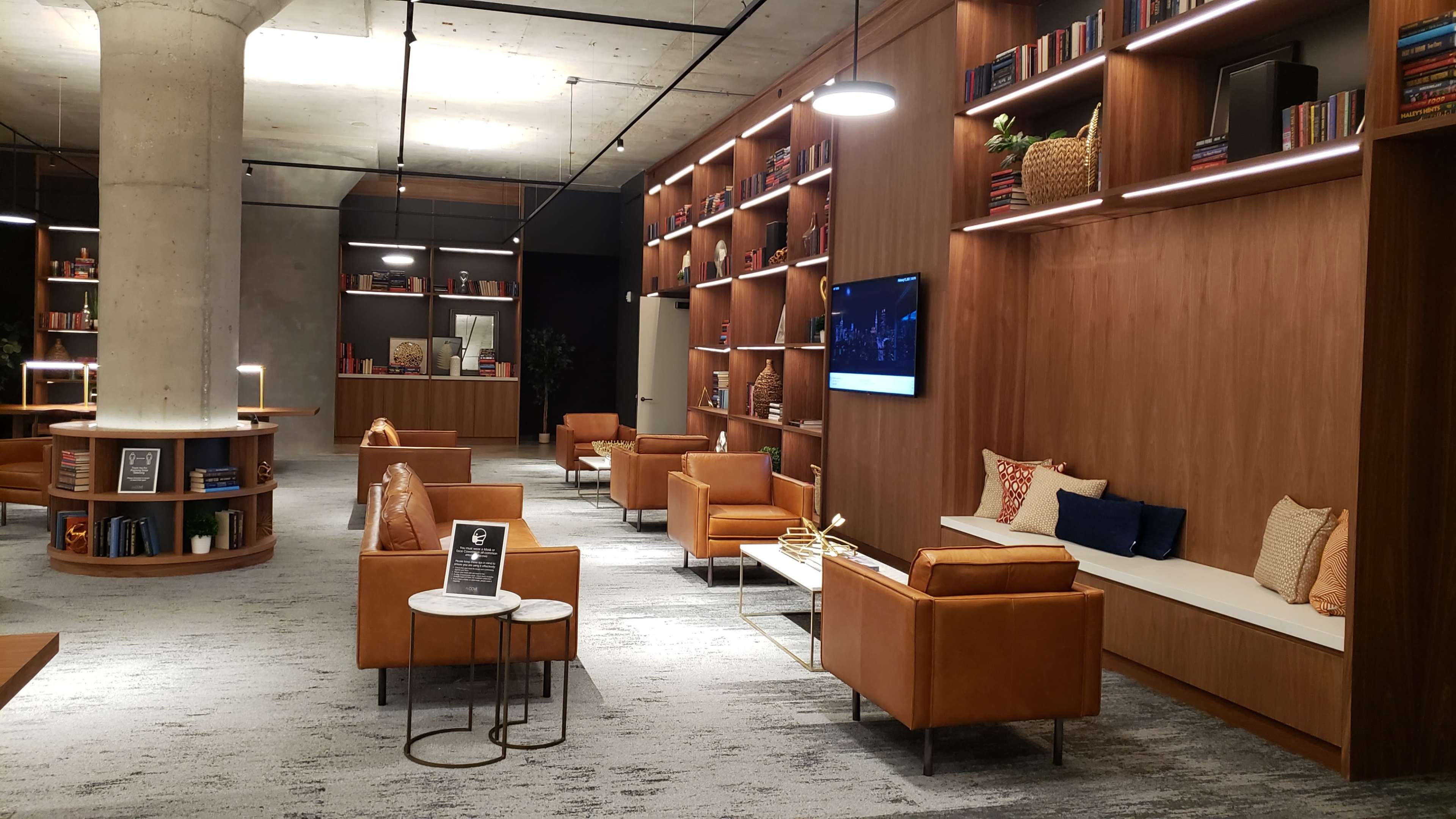 A modern lounge area with brown leather seating, wooden bookshelves, and a television mounted on the wall.
