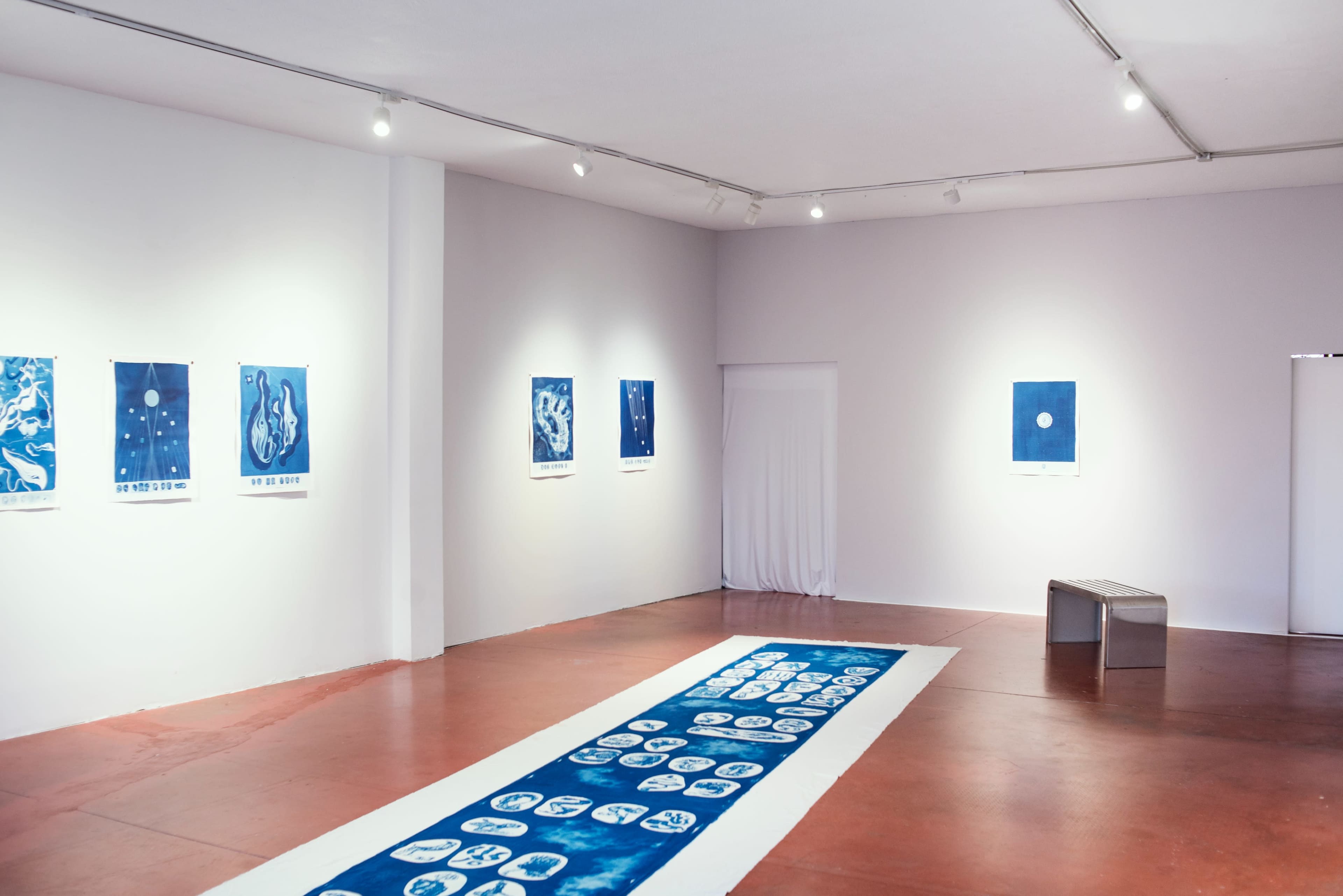 The image shows a spacious art gallery with blue-toned artworks displayed on the walls and a long blue runner on the floor.