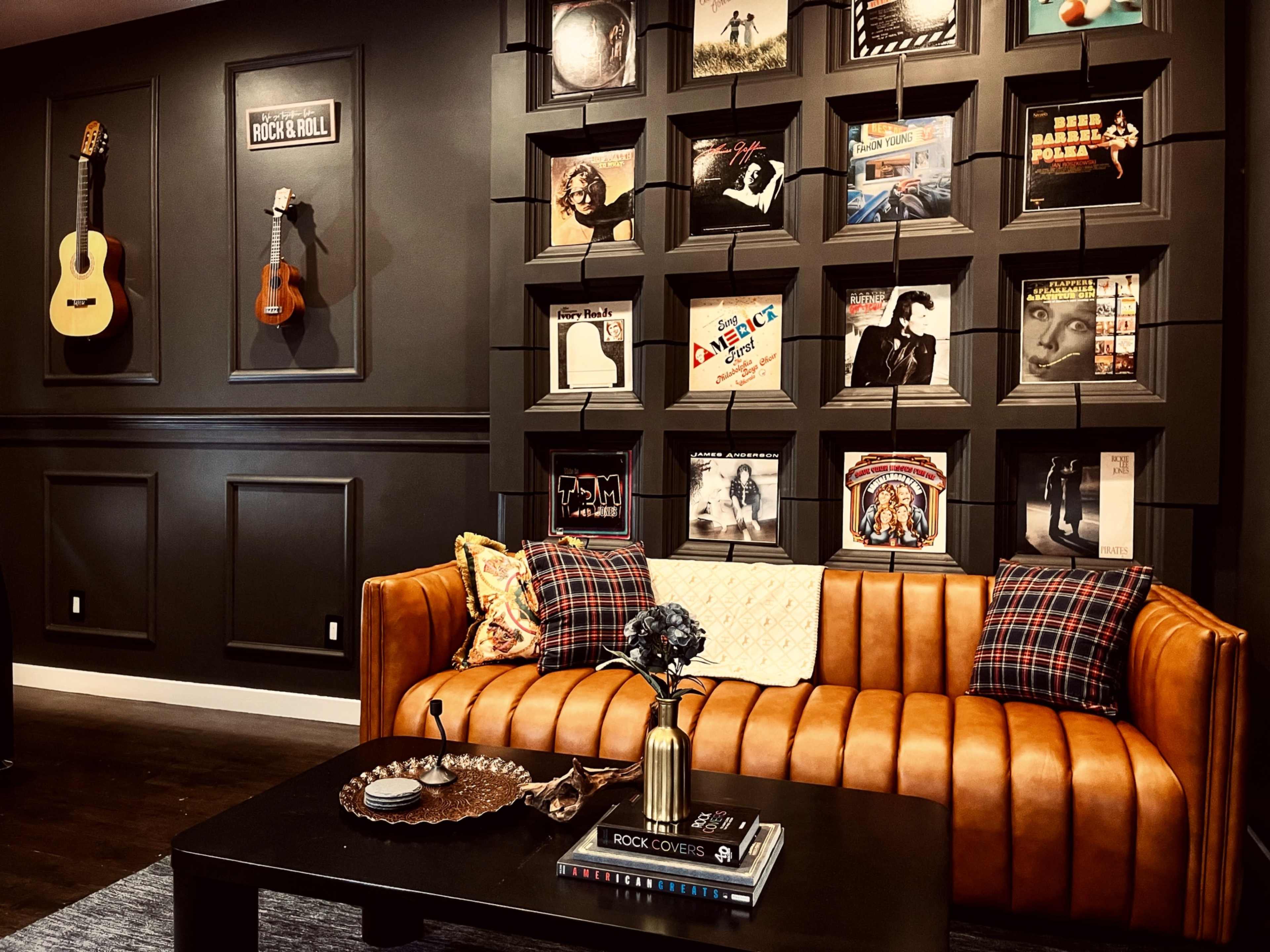 A stylish living room with a brown leather couch, a coffee table, and a wall display of framed records and guitars.