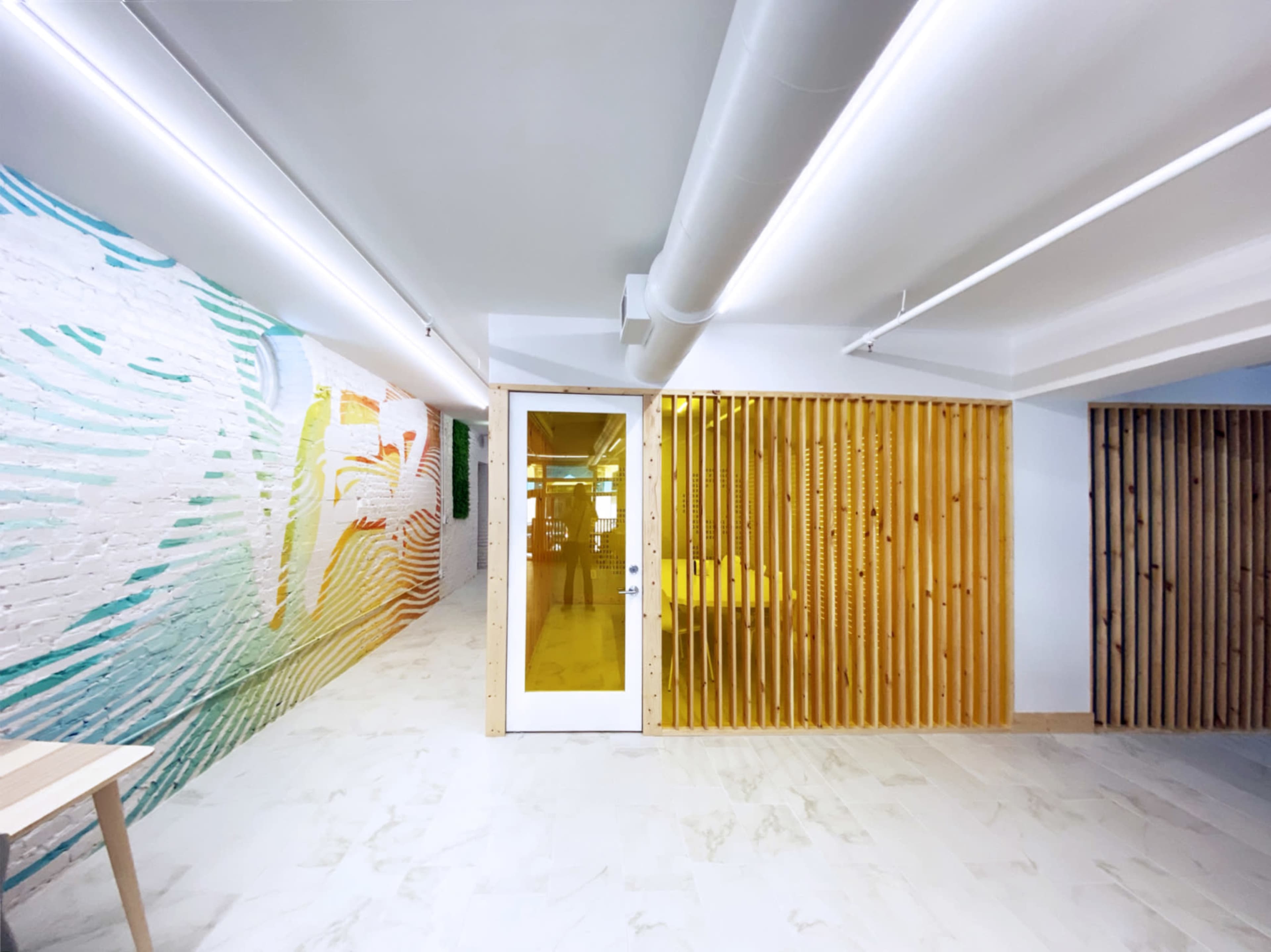 A modern interior space featuring a vibrant mural on one wall and a wooden slat partition next to a glass door.