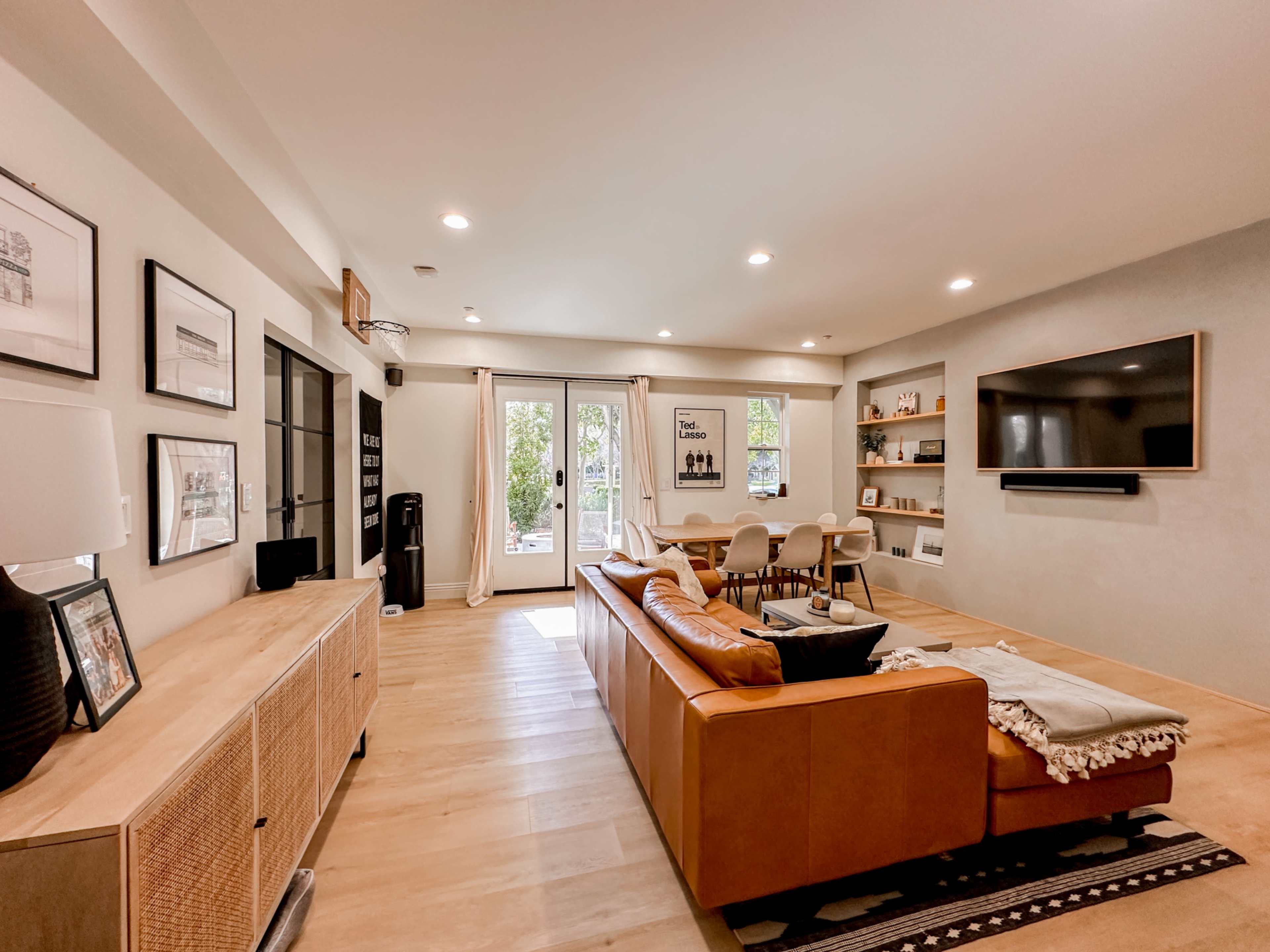 A modern living room with a brown leather sofa, a large television mounted on the wall, and glass doors leading to an outdoor area.