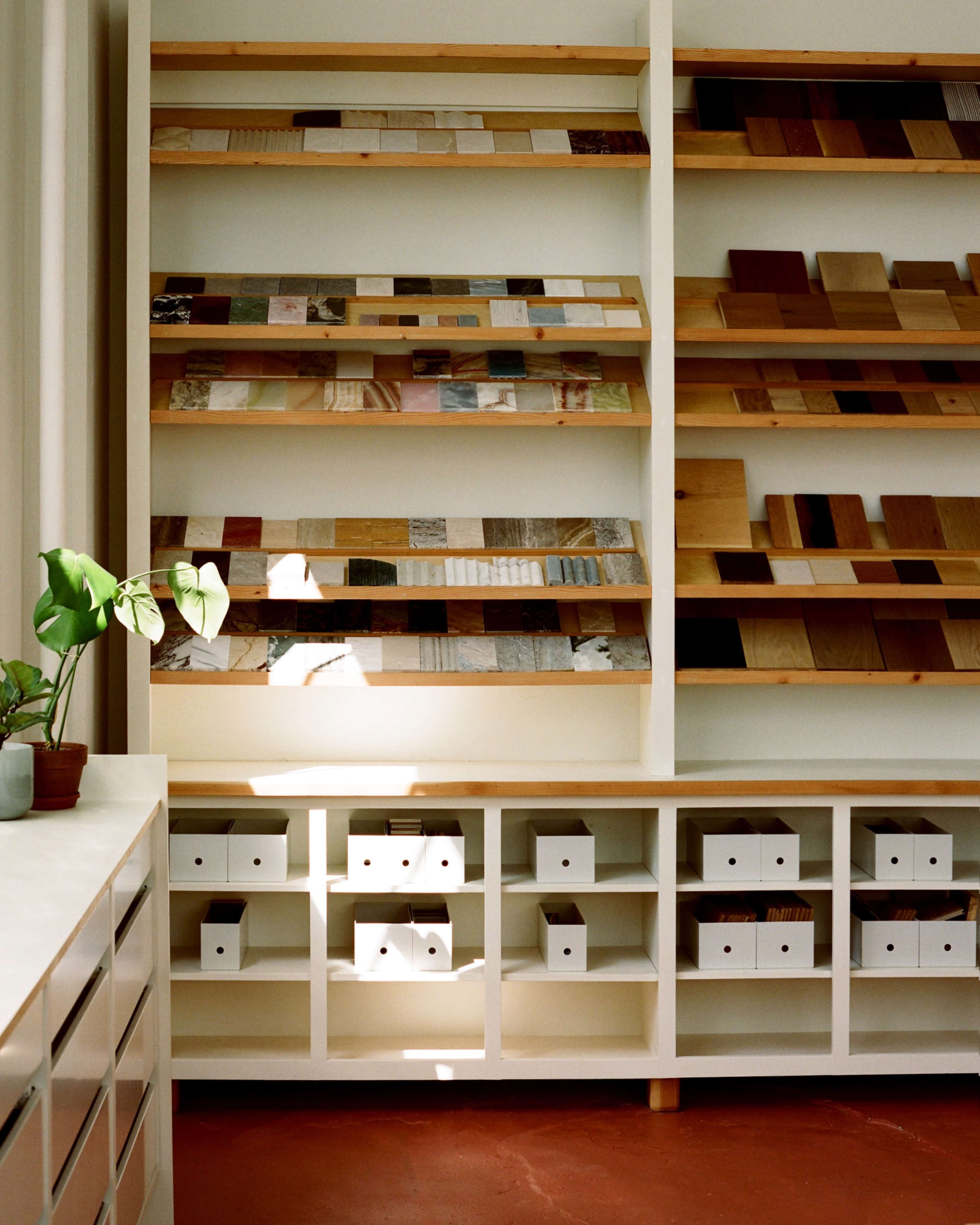 A bright room showcases a wall of wooden samples on shelves, with neatly arranged storage boxes beneath.