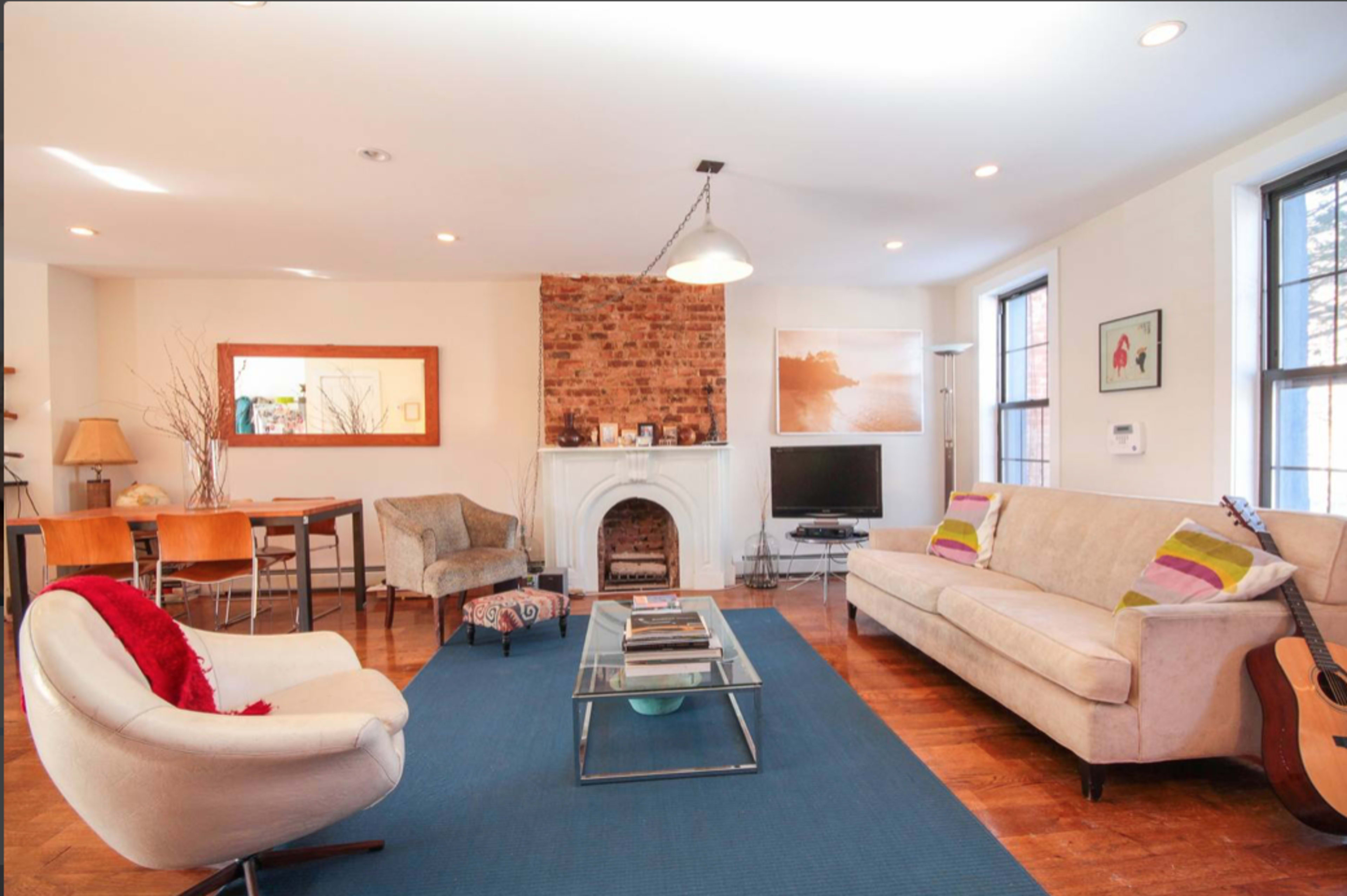 A cozy living room features a brick fireplace, two sofas, and a coffee table, with a guitar resting against one wall.