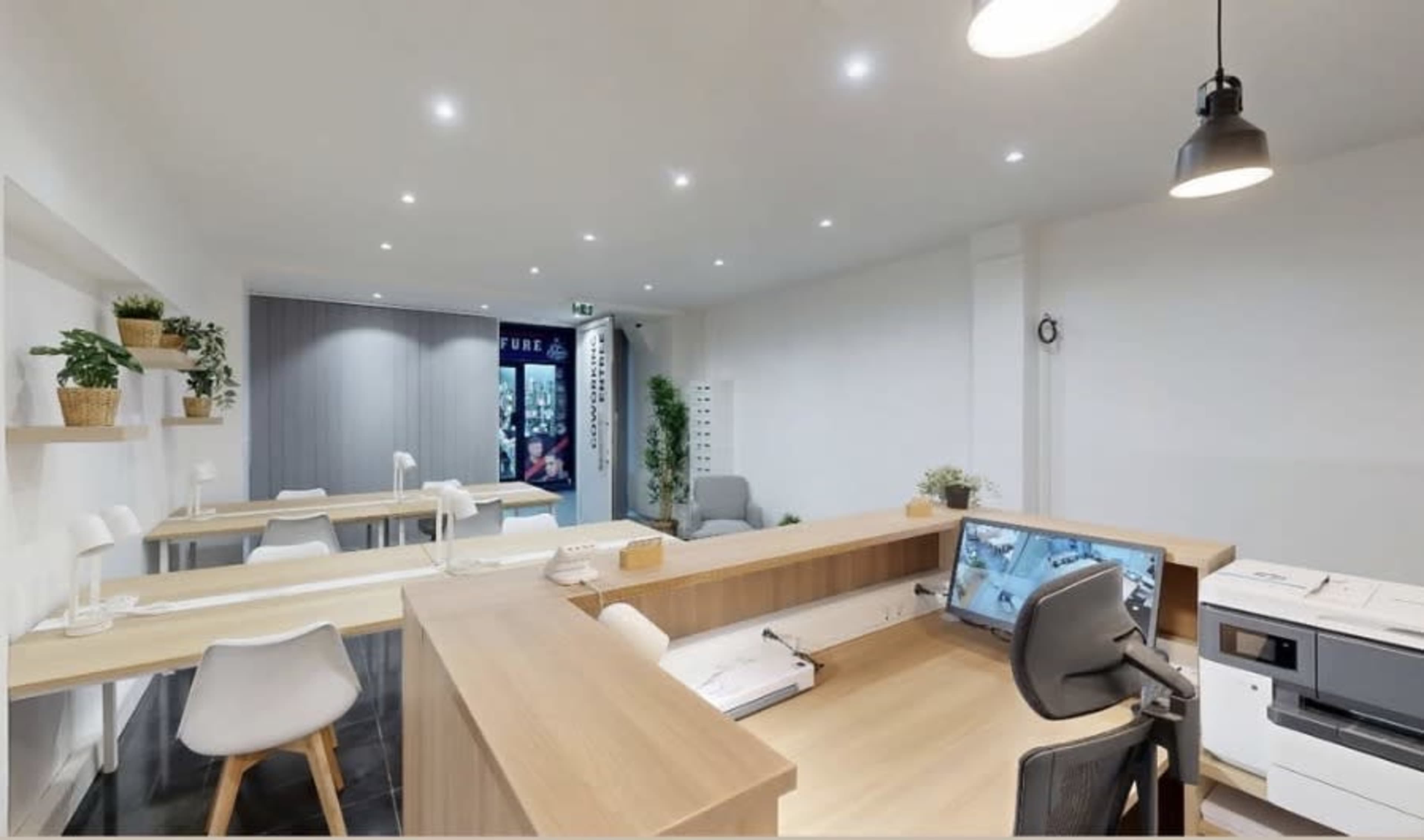 The image shows a modern office reception area with wooden desks, white chairs, and potted plants.