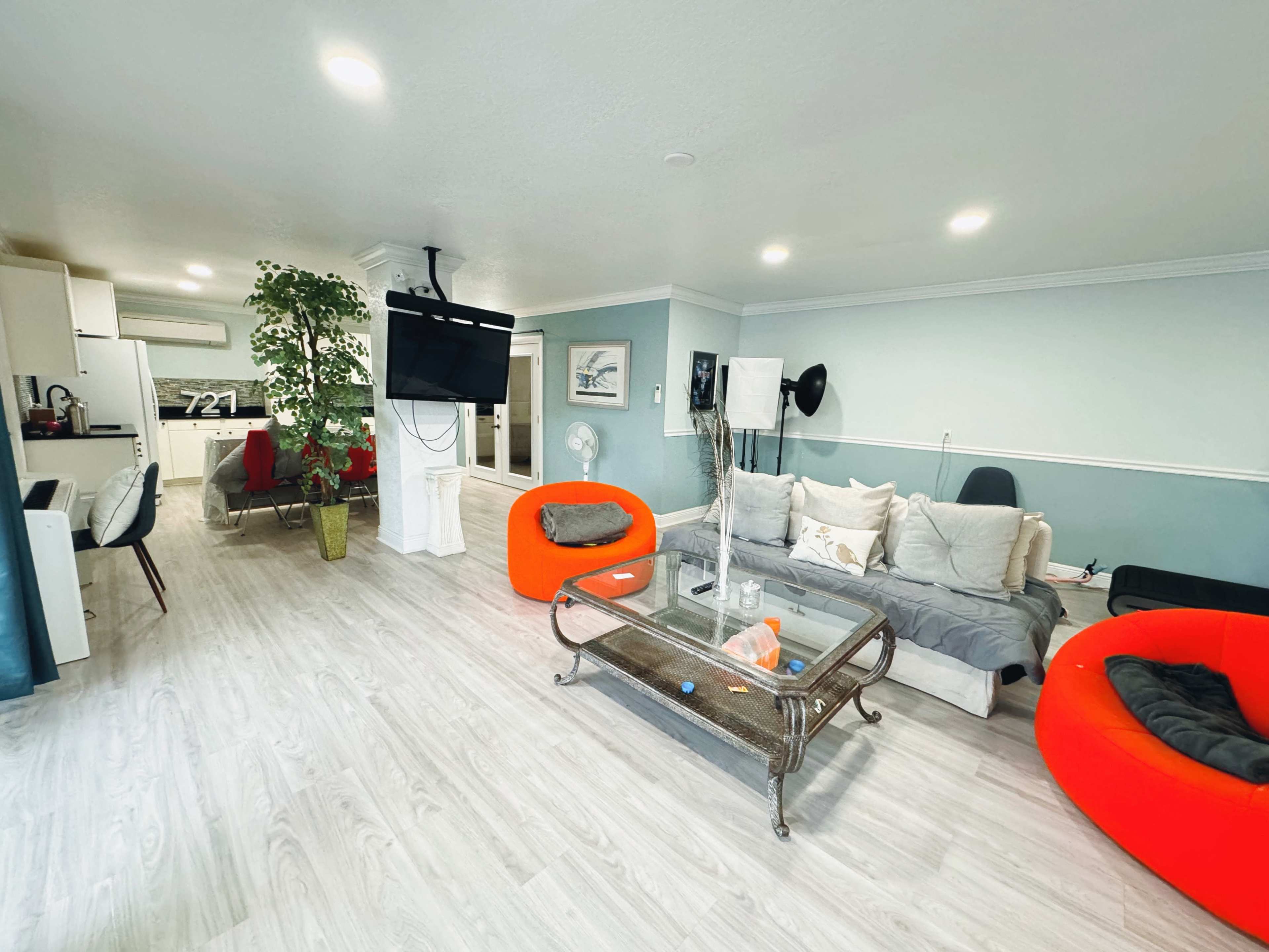 A modern living room with orange bean bag chairs, a glass coffee table, and a large television mounted on the wall.