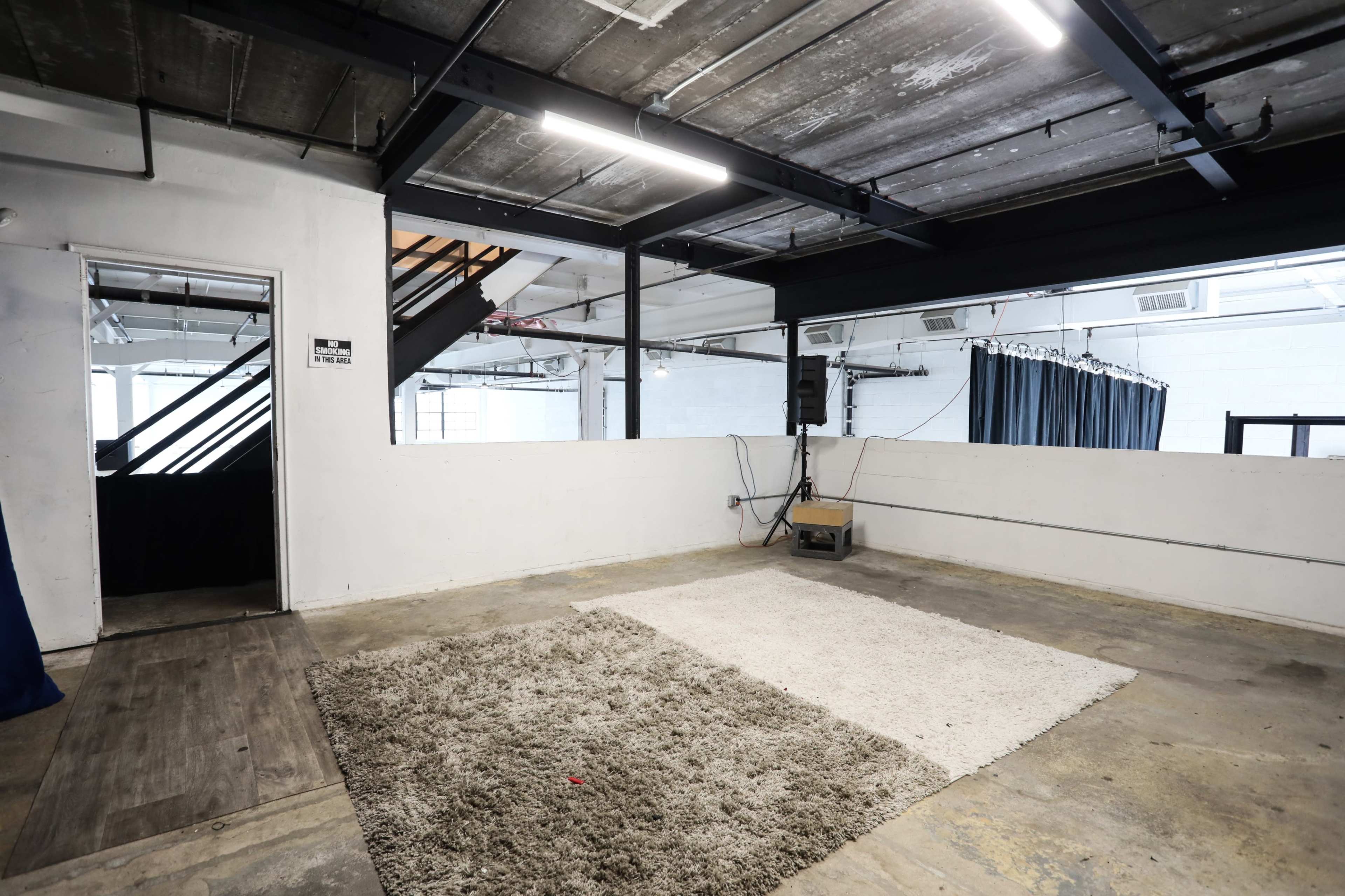 An empty industrial-style room with two area rugs on the floor and exposed beams above.