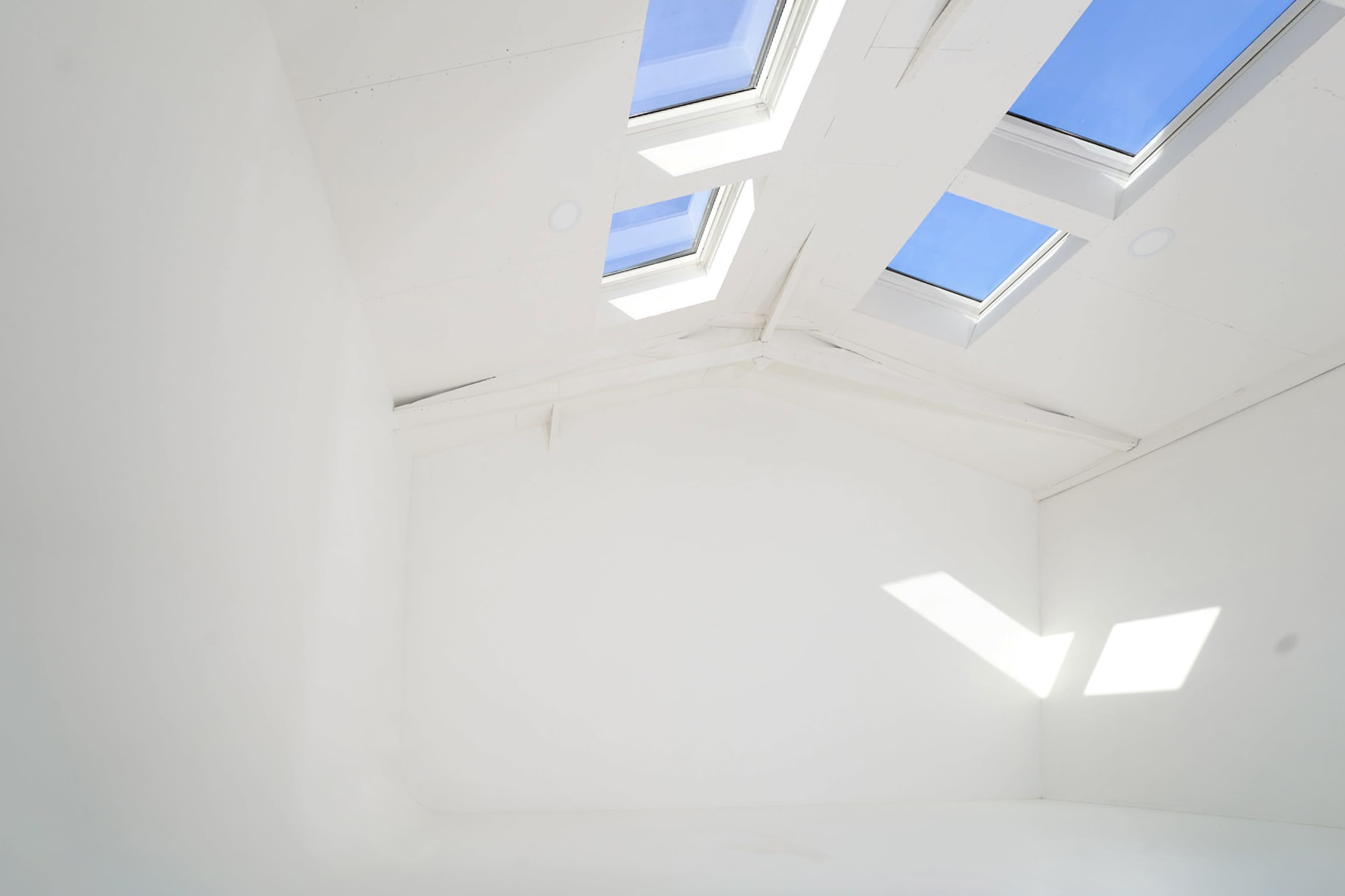 A bright, empty room features a sloped ceiling with multiple skylights allowing natural light to flood in.