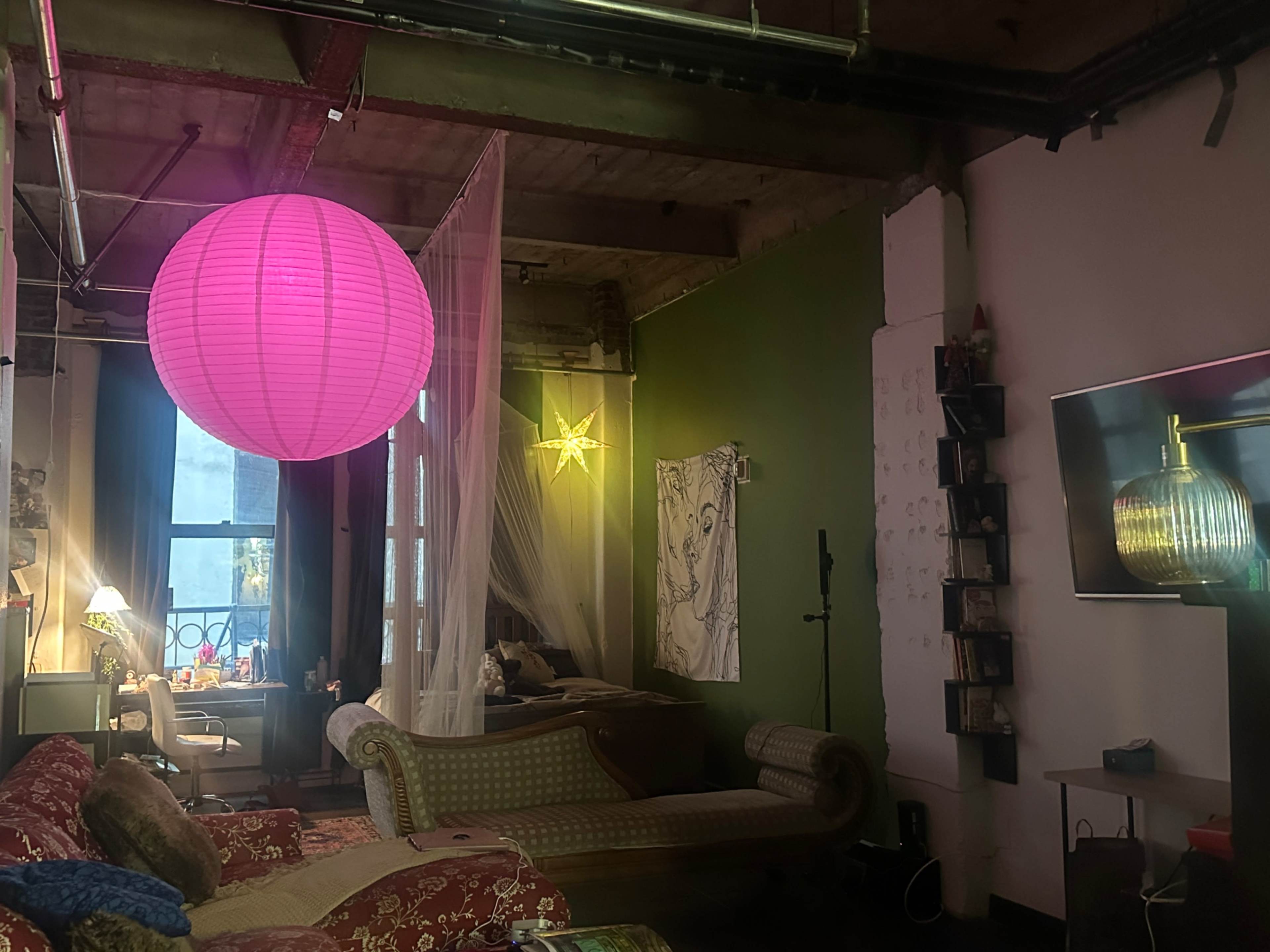 The image shows a spacious loft-style living area featuring a pink paper lantern, a star-shaped light decoration, and a mix of modern and vintage furniture.