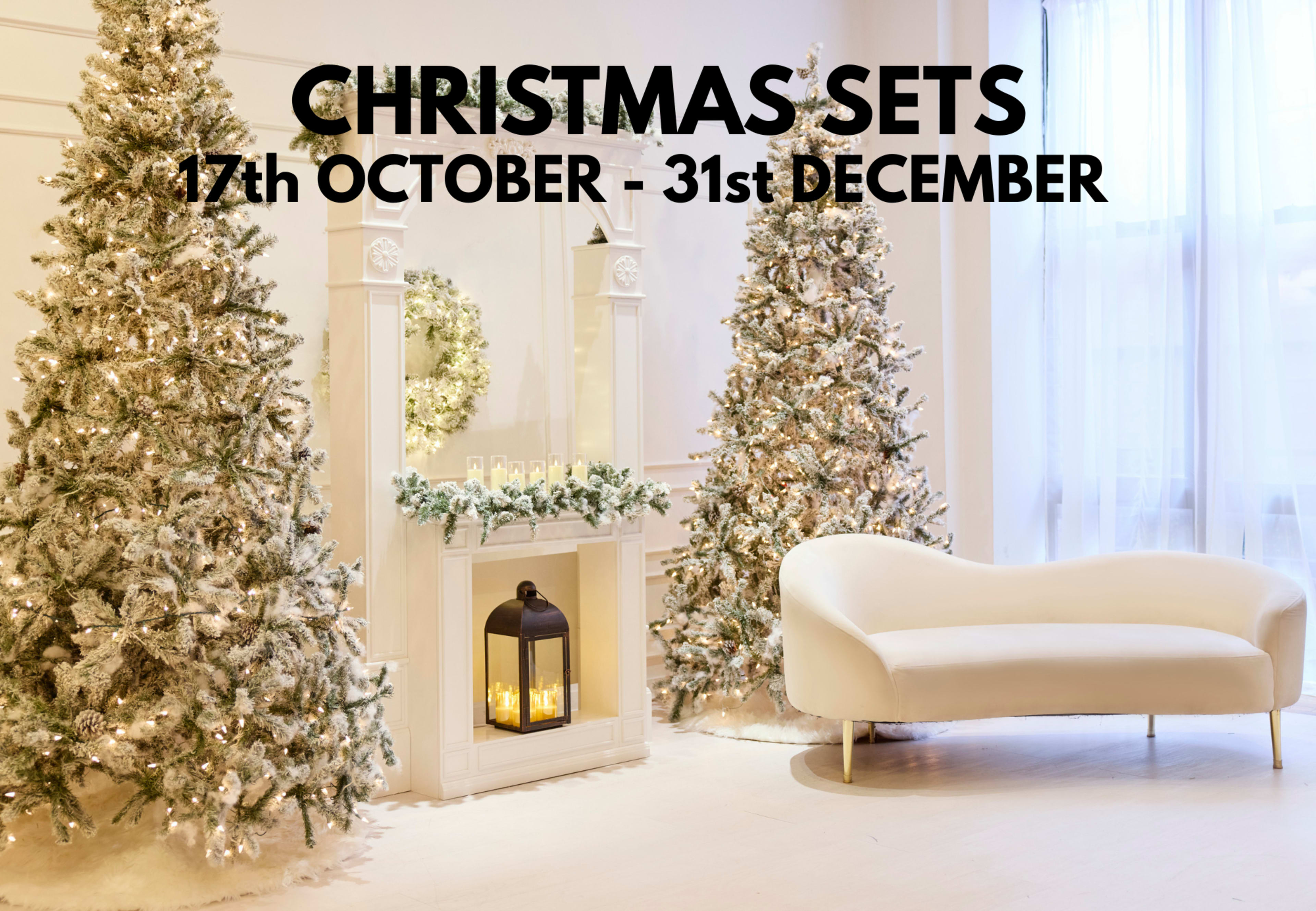 The image shows a festive room decorated with two snow-covered Christmas trees, a fireplace adorned with greenery, and a white sofa, along with a text overlay indicating Christmas sets available from October 17 to December 31.