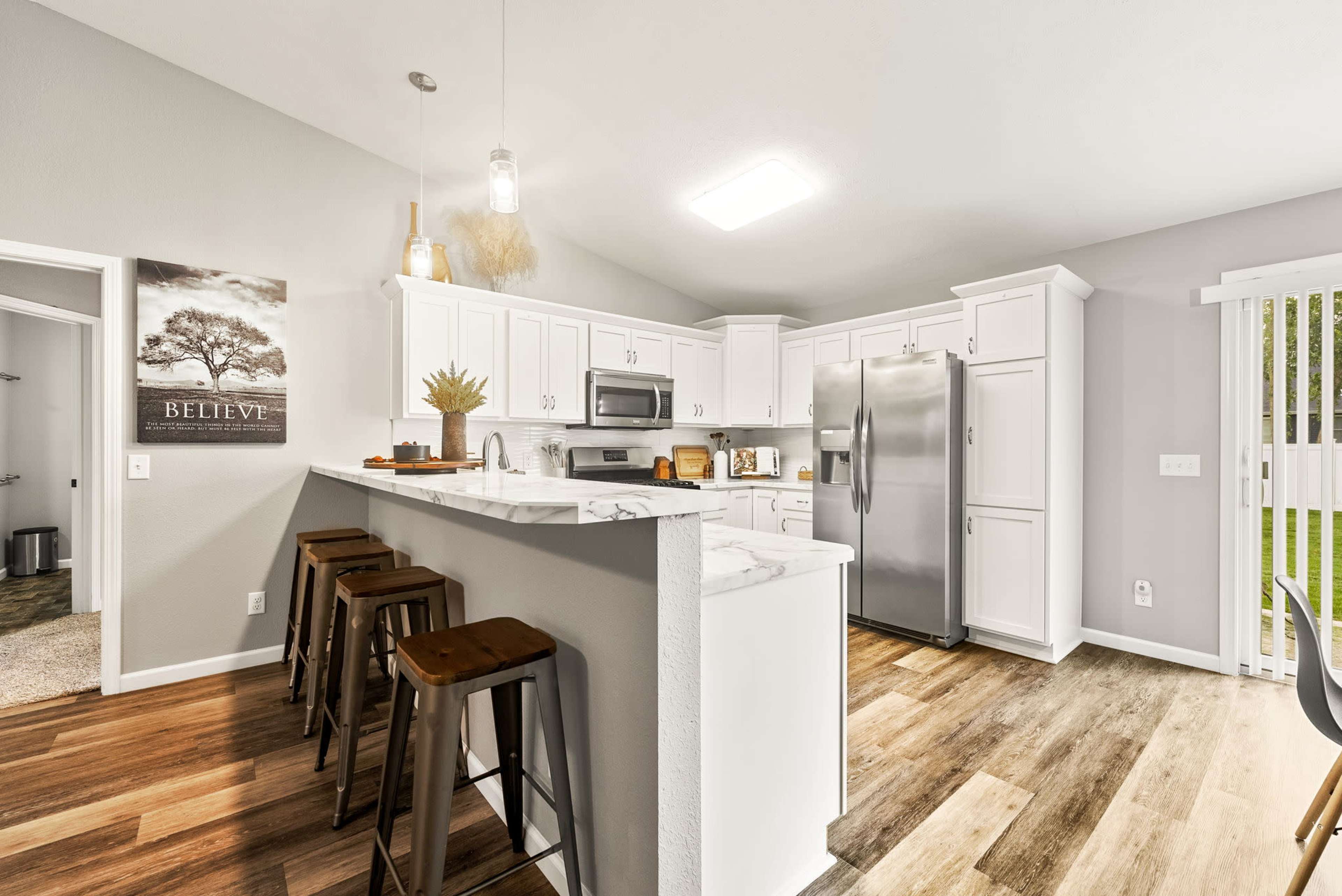 A modern kitchen with white cabinetry, stainless steel appliances, and wooden bar stools at a breakfast counter.