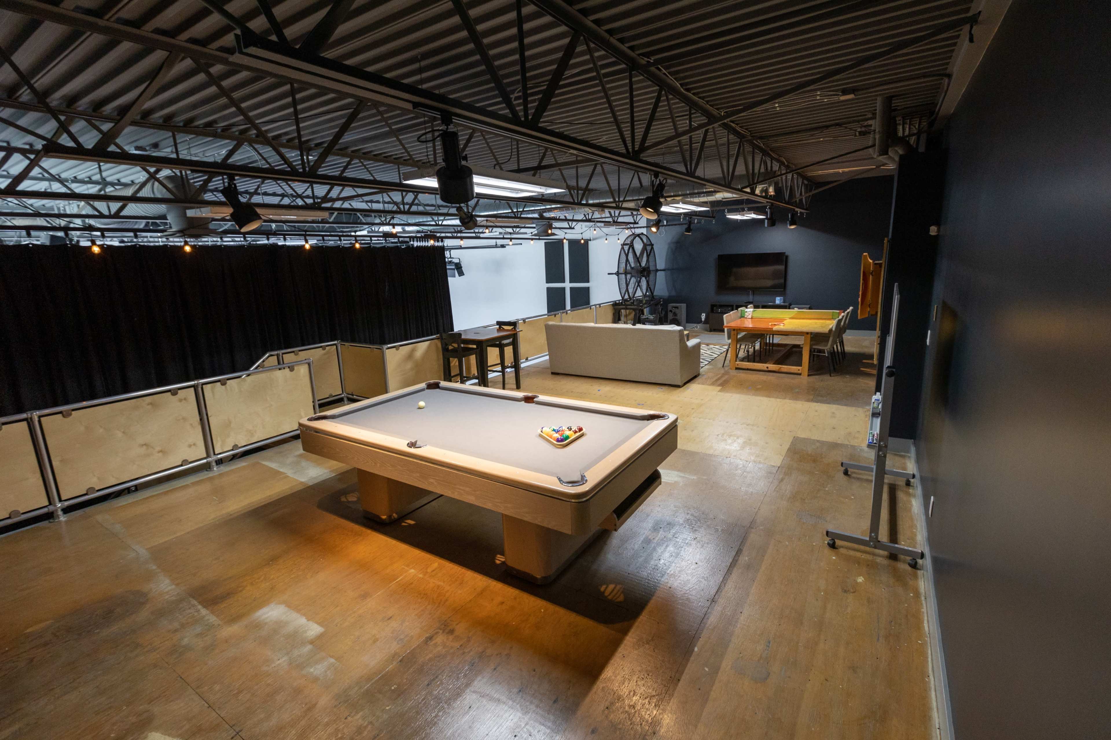 A game room with a pool table in the center, surrounded by seating areas and various recreational equipment.