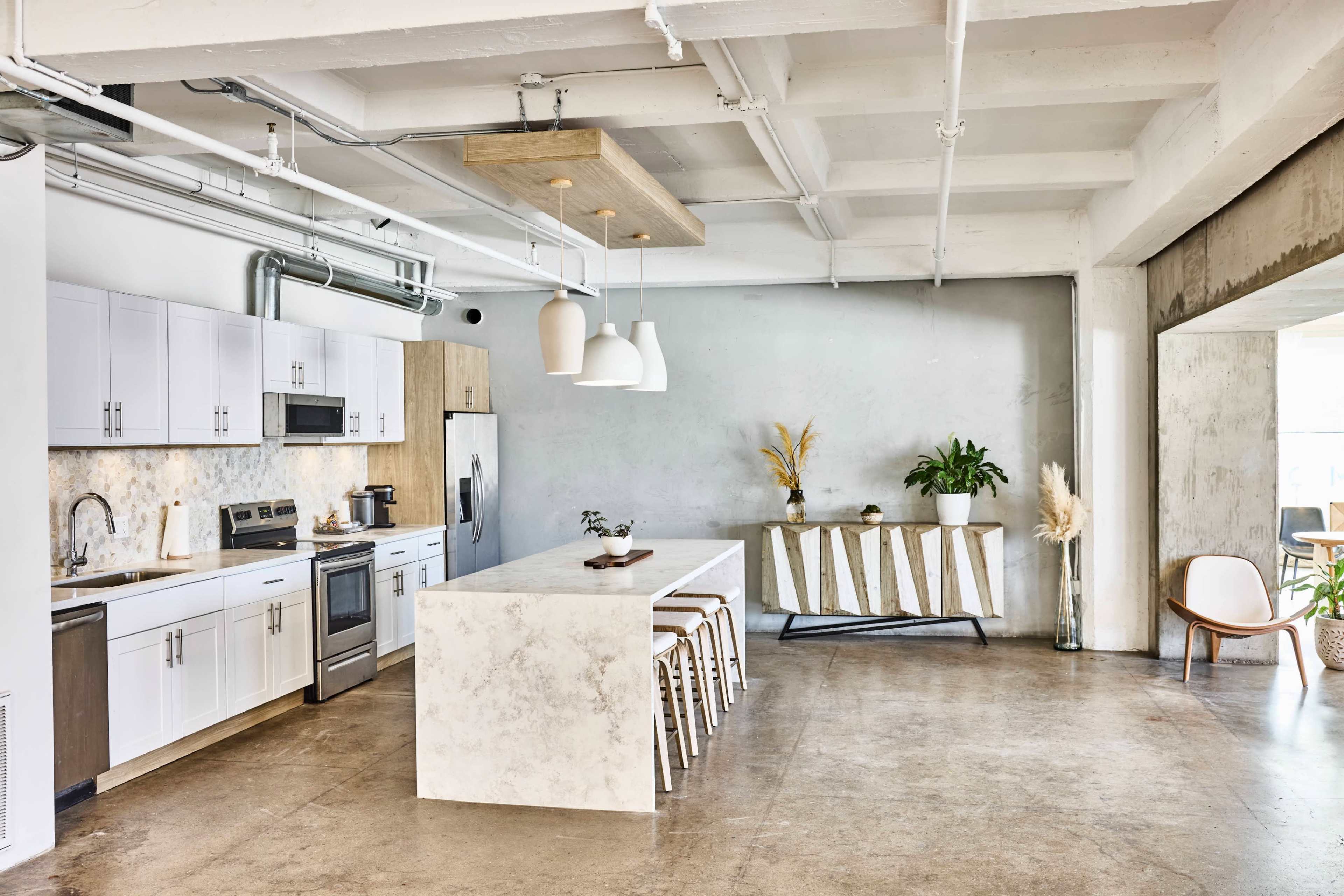 A modern kitchen features a large island with bar stools, stainless steel appliances, white cabinetry, and natural decor elements in a bright, open space.