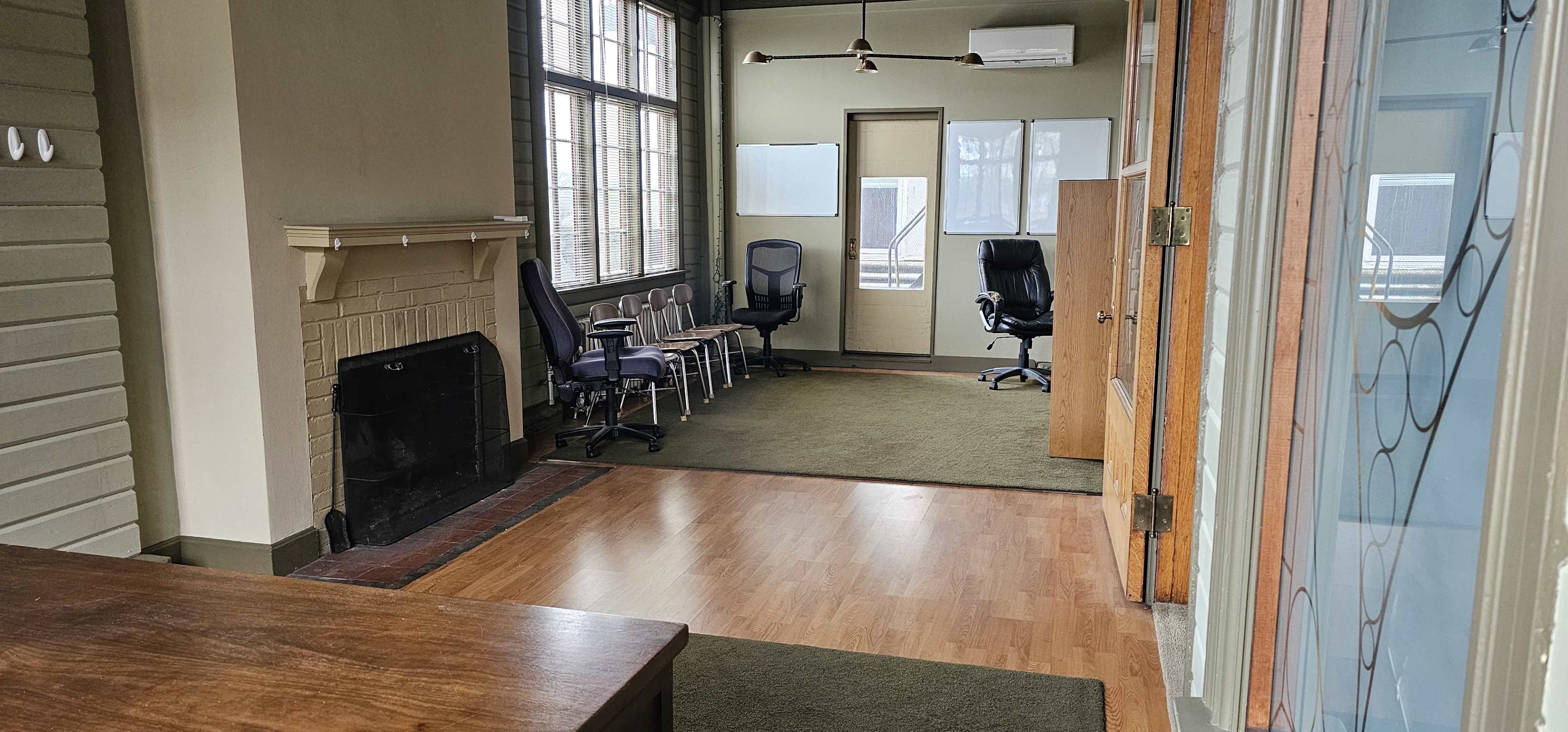 An empty office space with a fireplace, several chairs arranged against the wall, and two different seating areas.