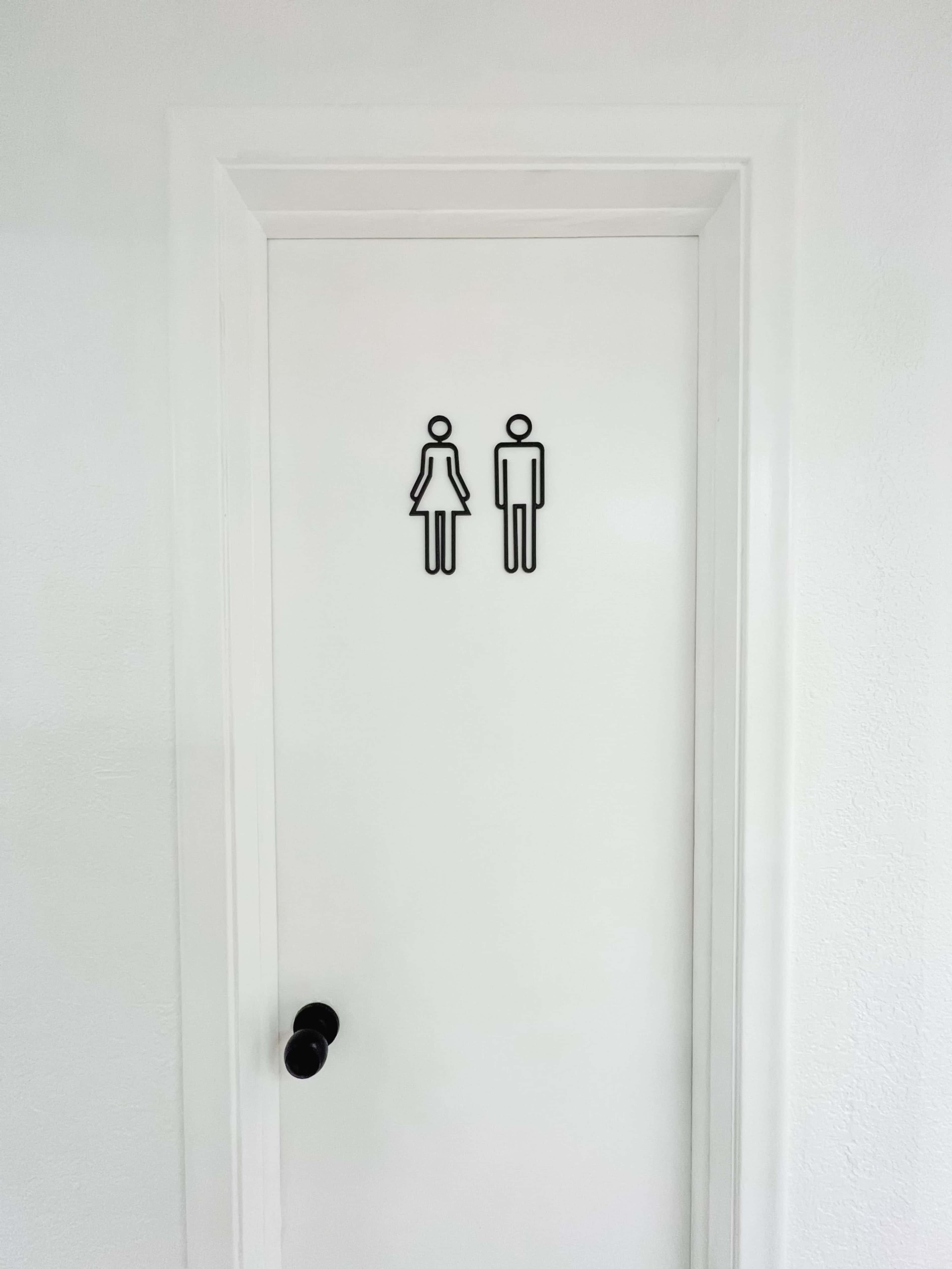 A white door featuring a black sign indicating a bathroom, with symbols representing male and female figures.