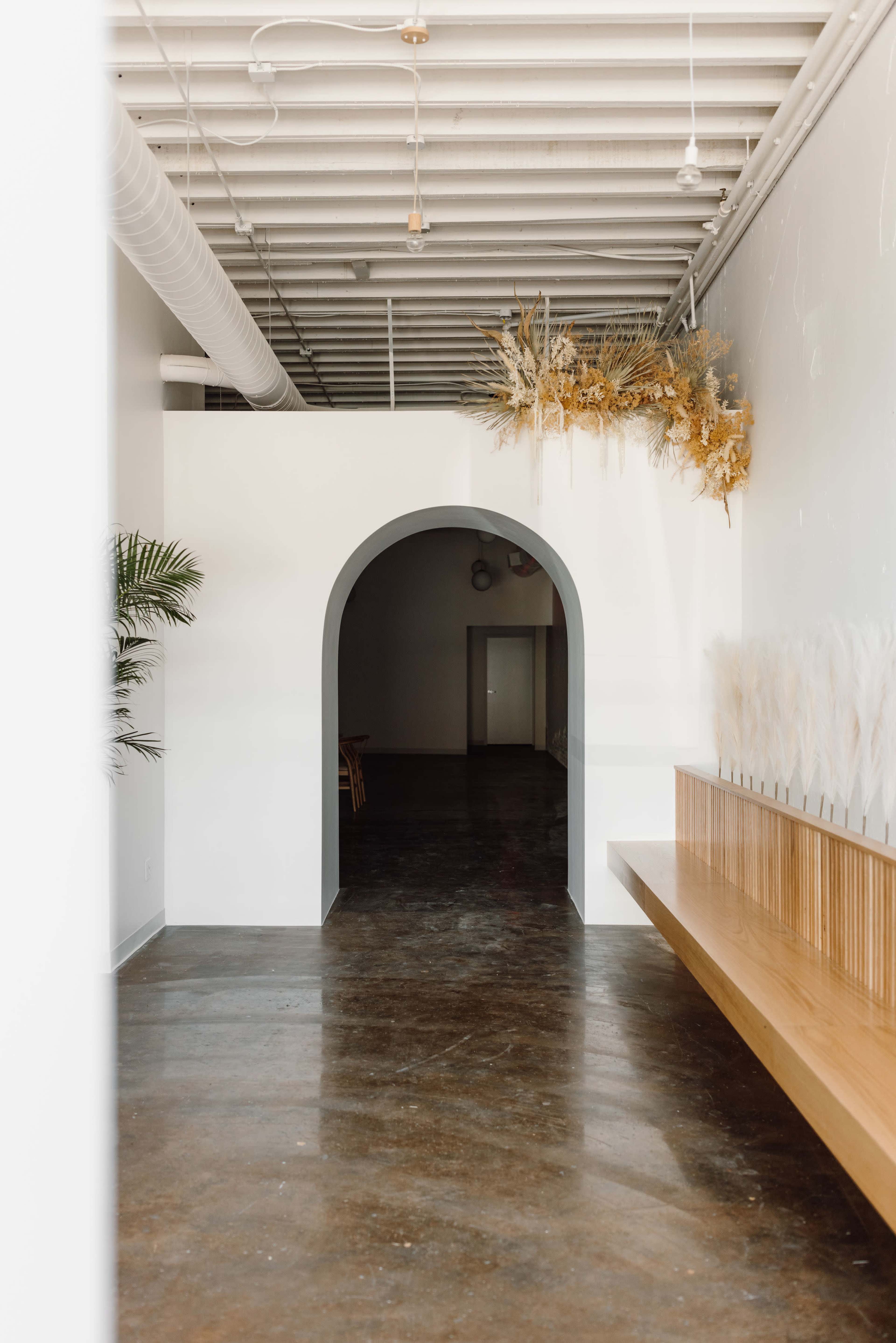 A modern interior space featuring an arched doorway, a wooden bench, and decorative dried plants above the entrance.