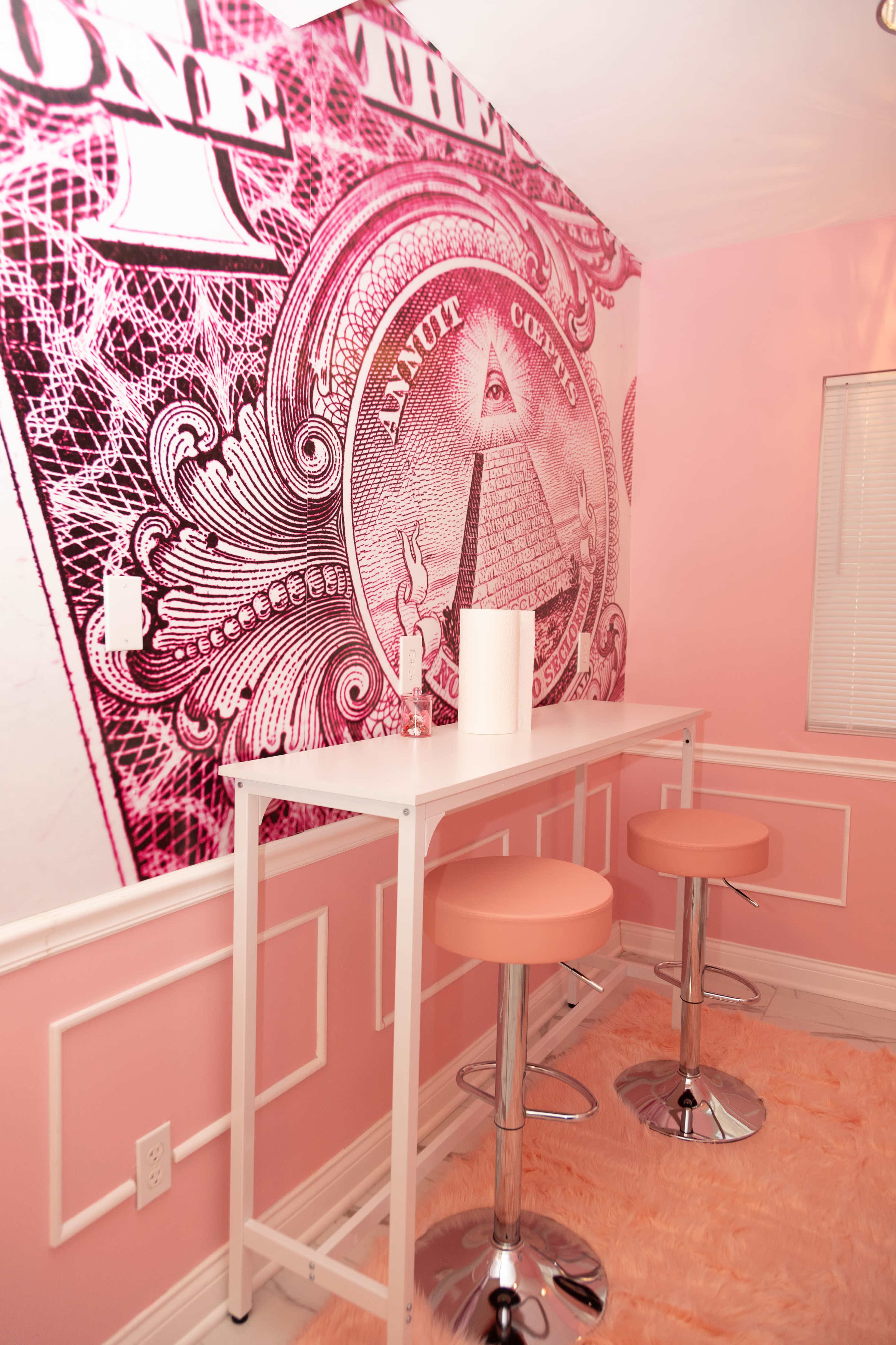 A small modern bar area with two pink stools in front of a wall featuring a large dollar bill design.