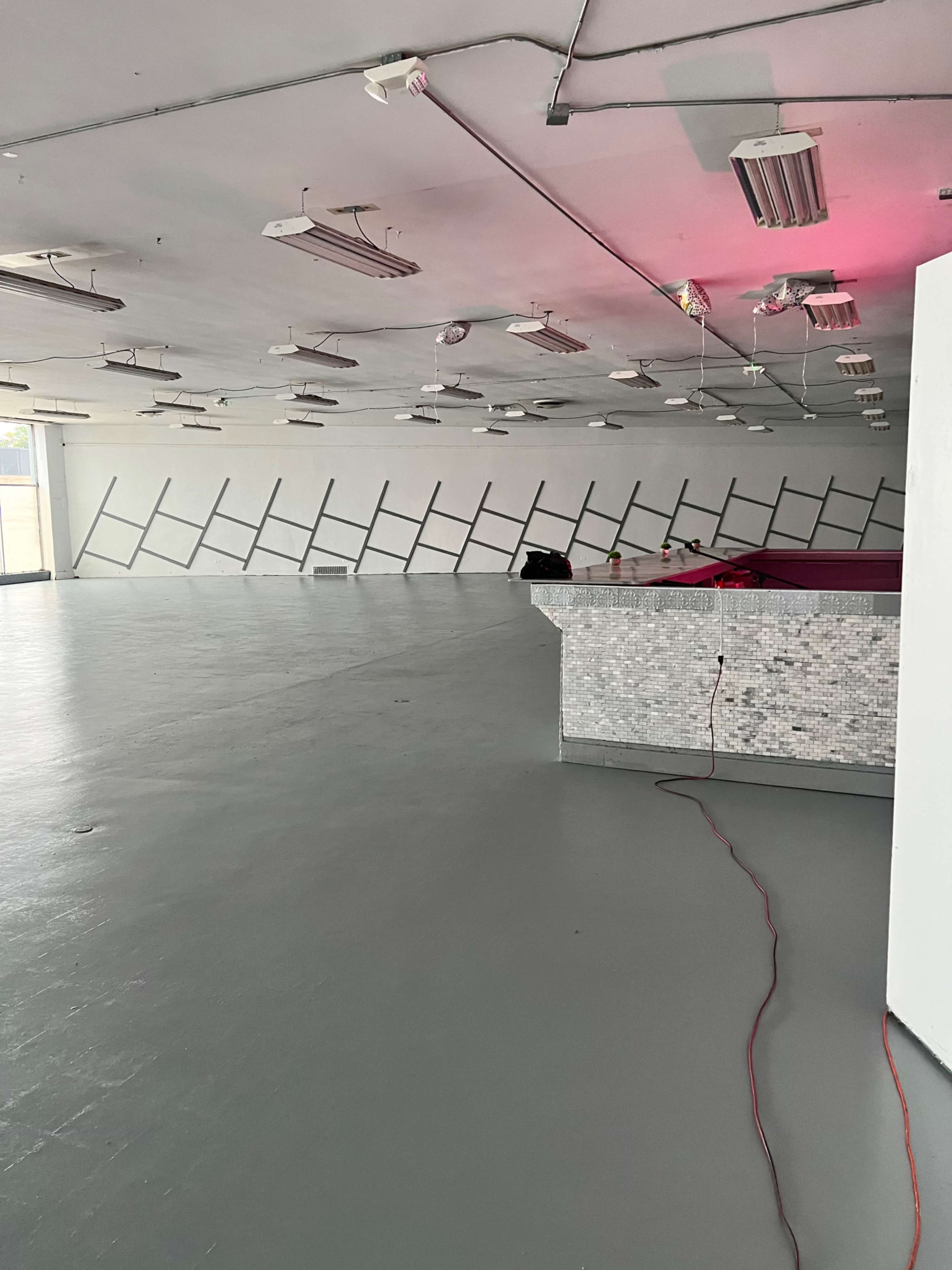A spacious, empty room with a gray floor and a mirrored bar counter, featuring a diagonal pattern on the walls.