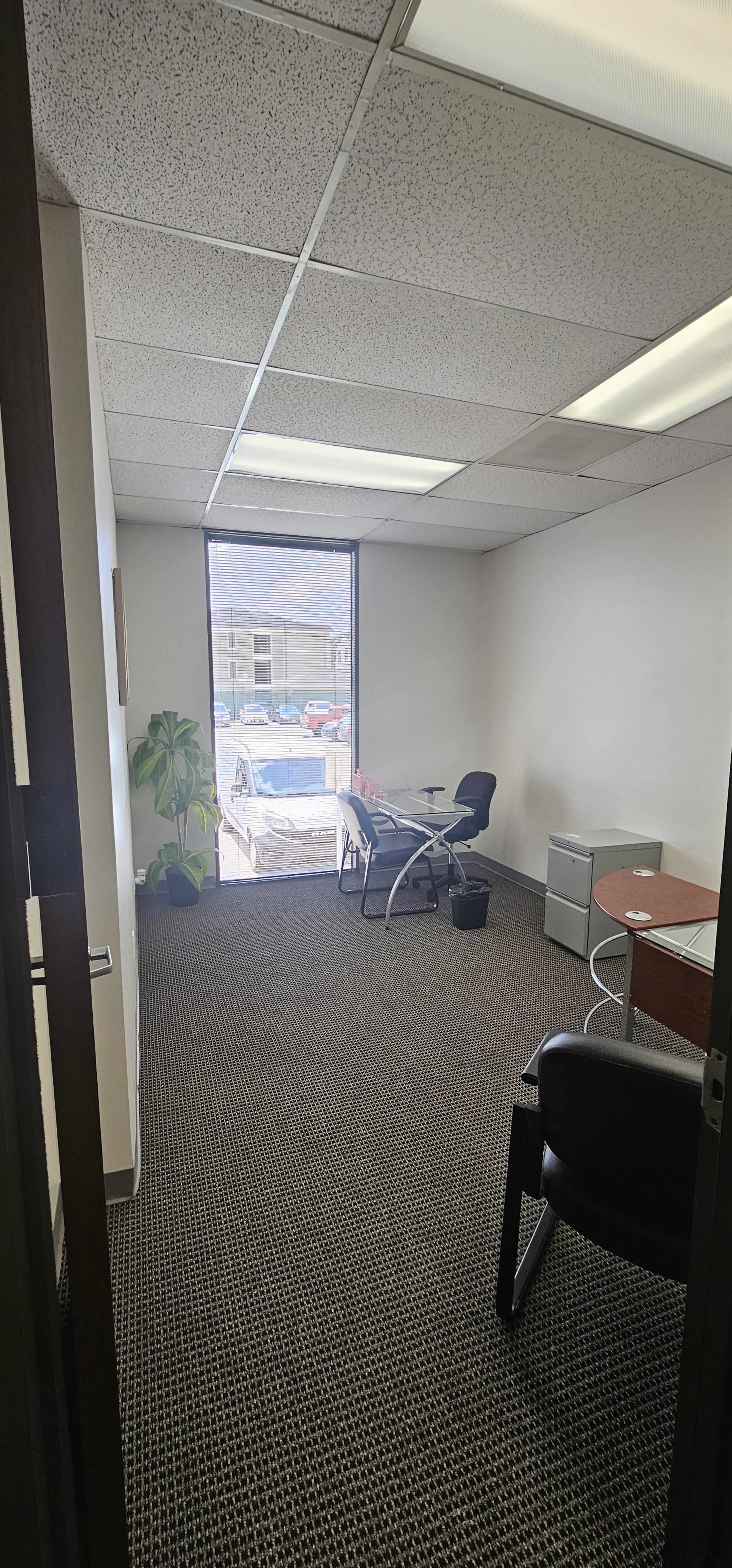 The image shows a small office space with two chairs, a table, and a window providing a view of an outdoor area.