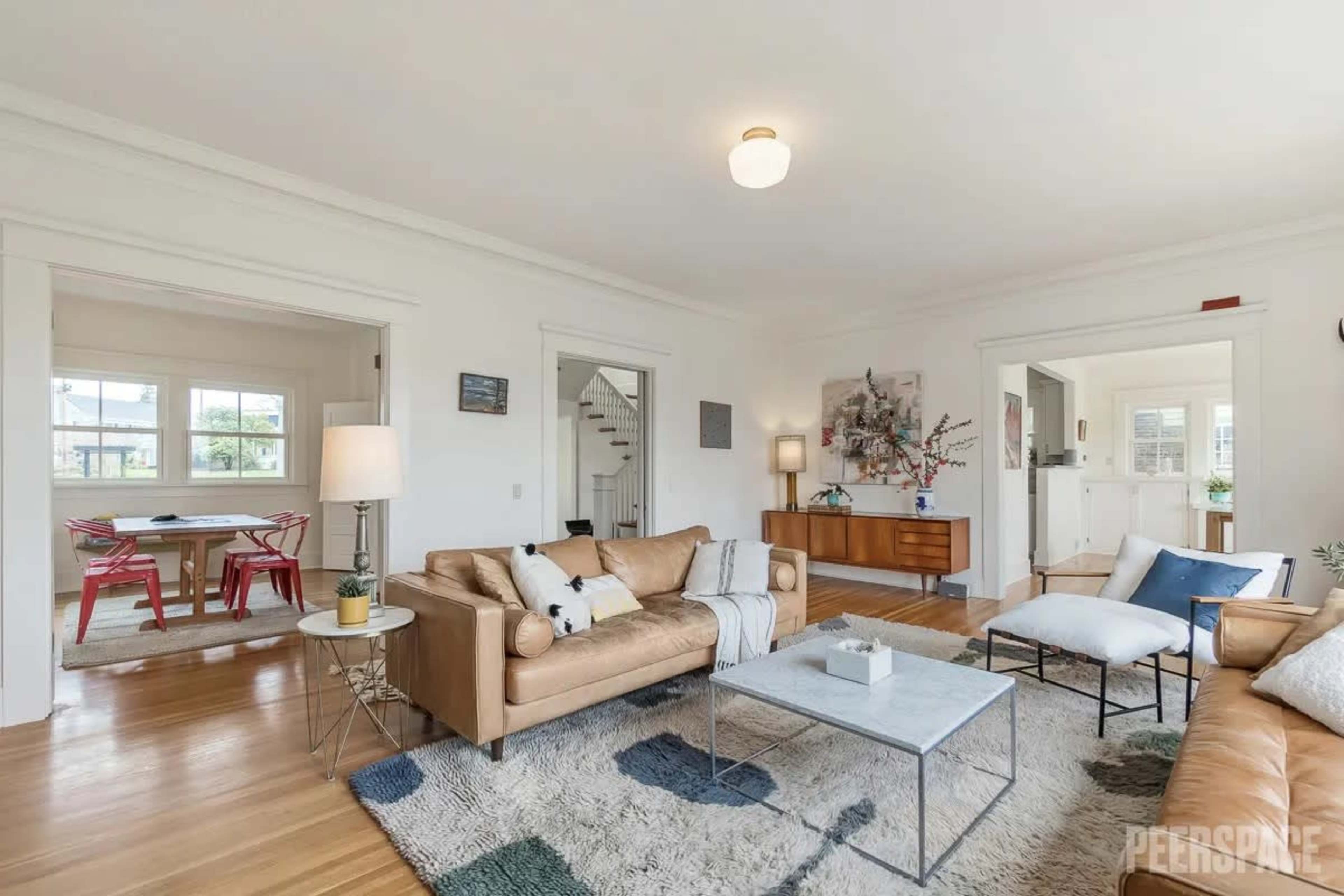 A brightly lit living room featuring a tan leather sofa, a coffee table, and adjacent dining space visible through an open doorway.