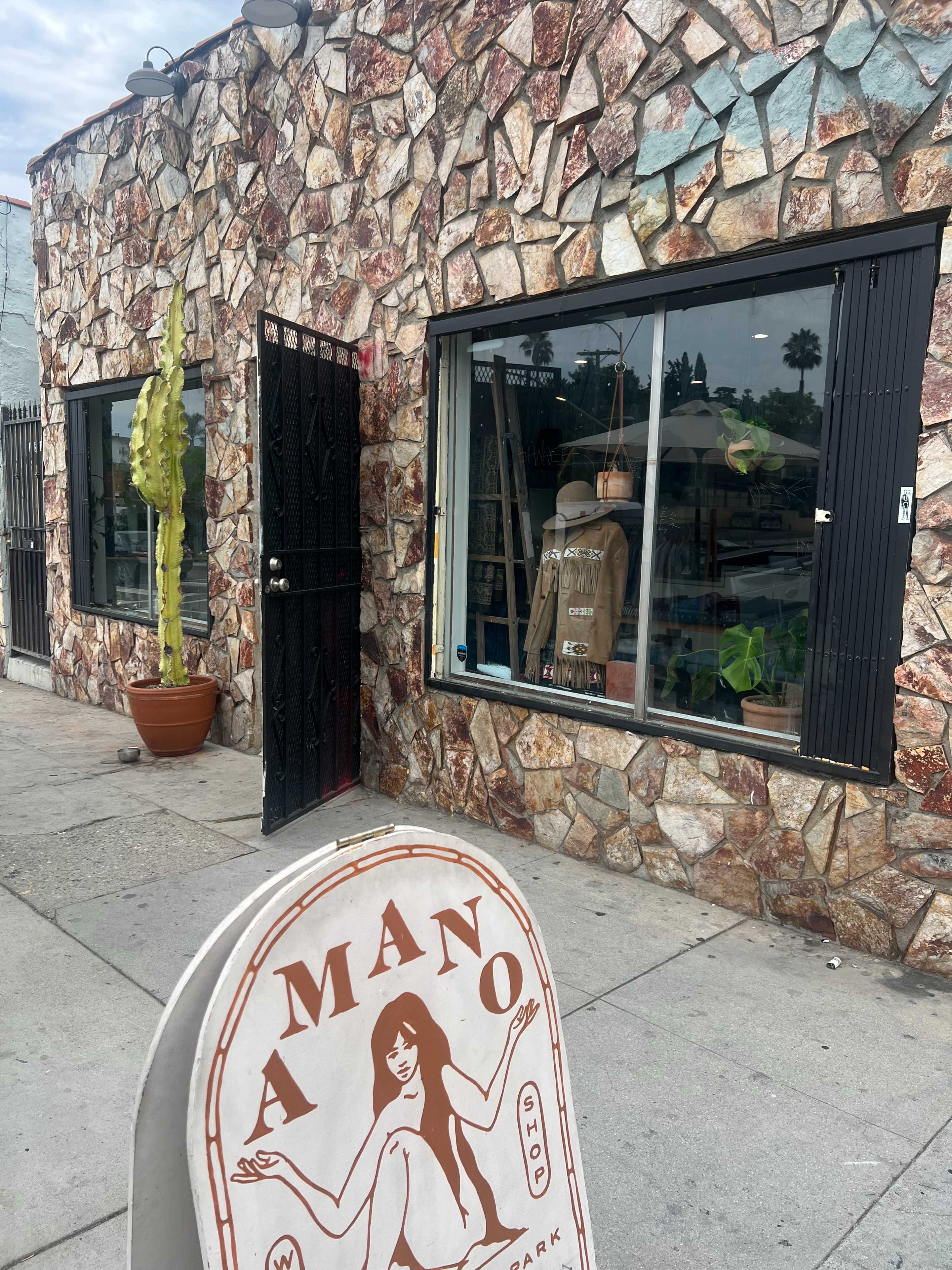 A storefront with a stone exterior features large windows displaying various plants and a sign that reads "AMANO."