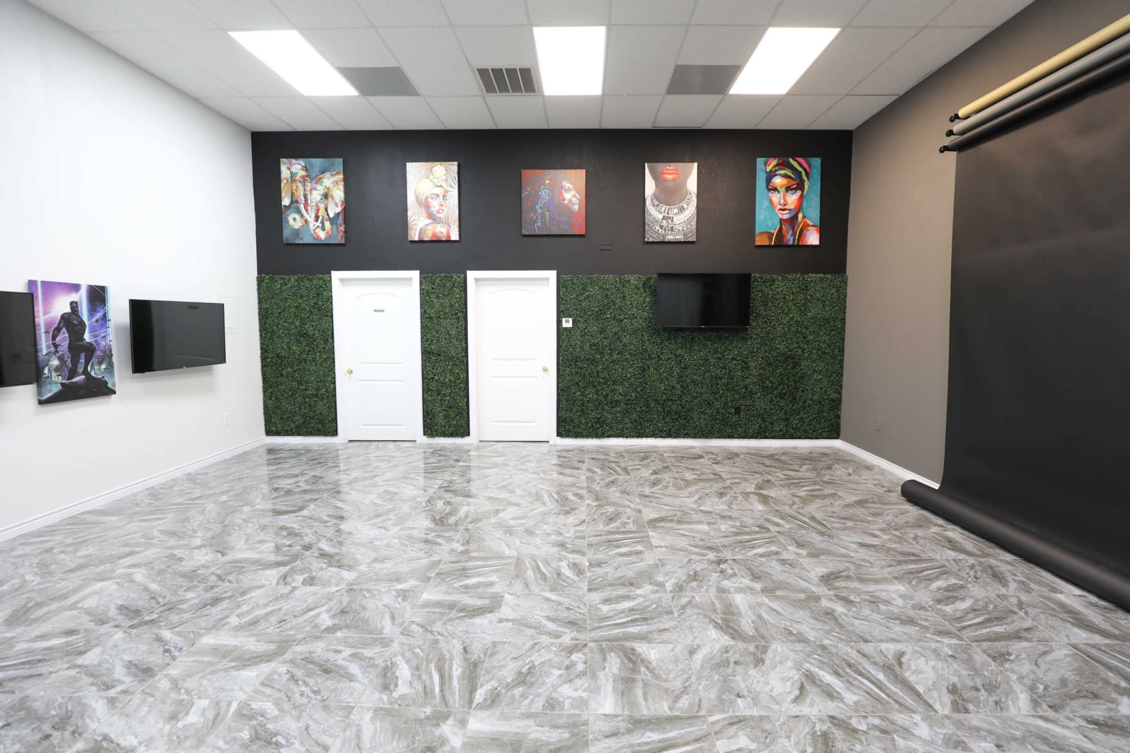A spacious room with a polished floor, two doors on a green accent wall, framed artwork, and a black photographic backdrop.